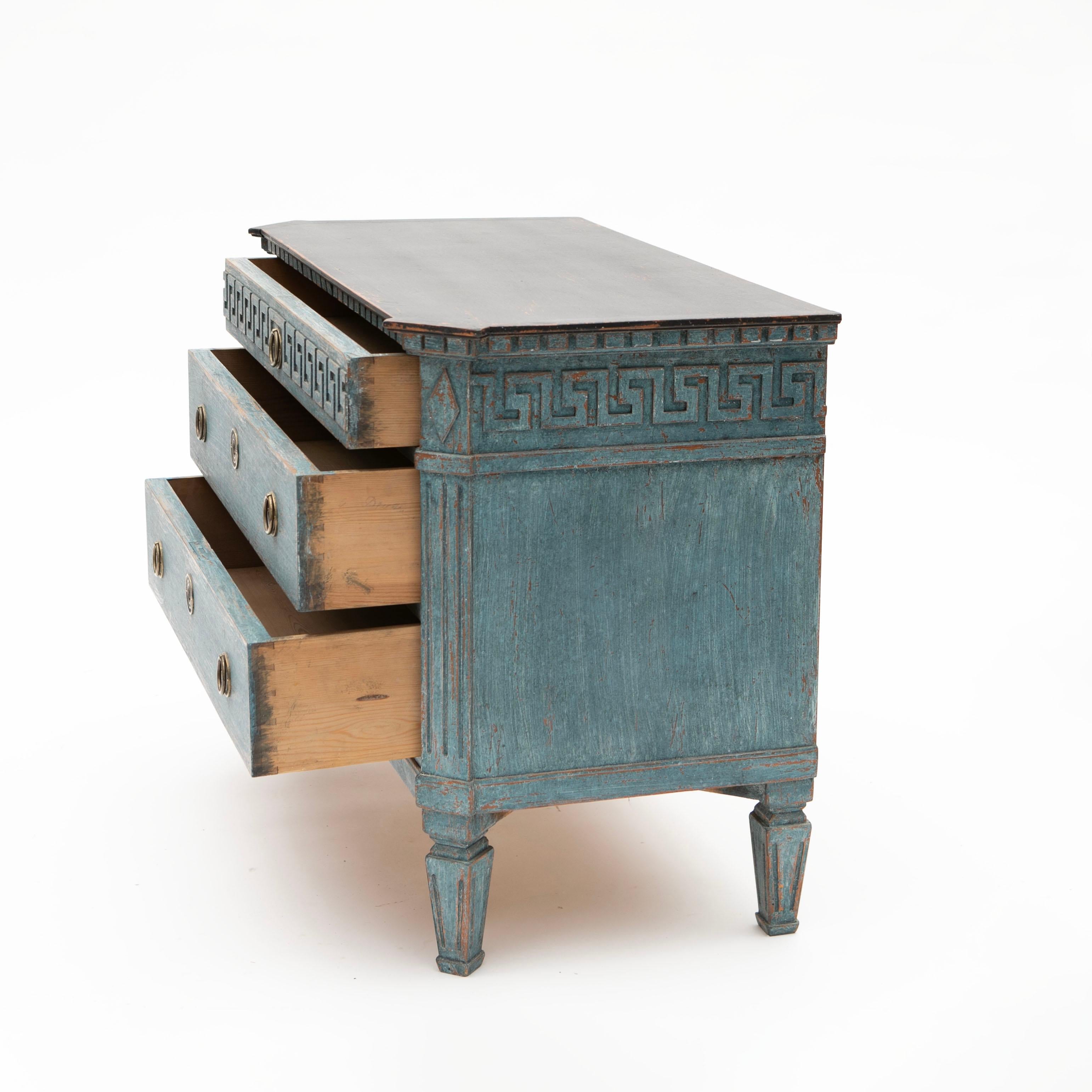 A pair of antique Swedish Gustavian style blue painted chest of three drawers, dating from the 19th century.
Each chest features a black painted rectangular top with canted corners in the front, sitting above a delicate meander décor molding running
