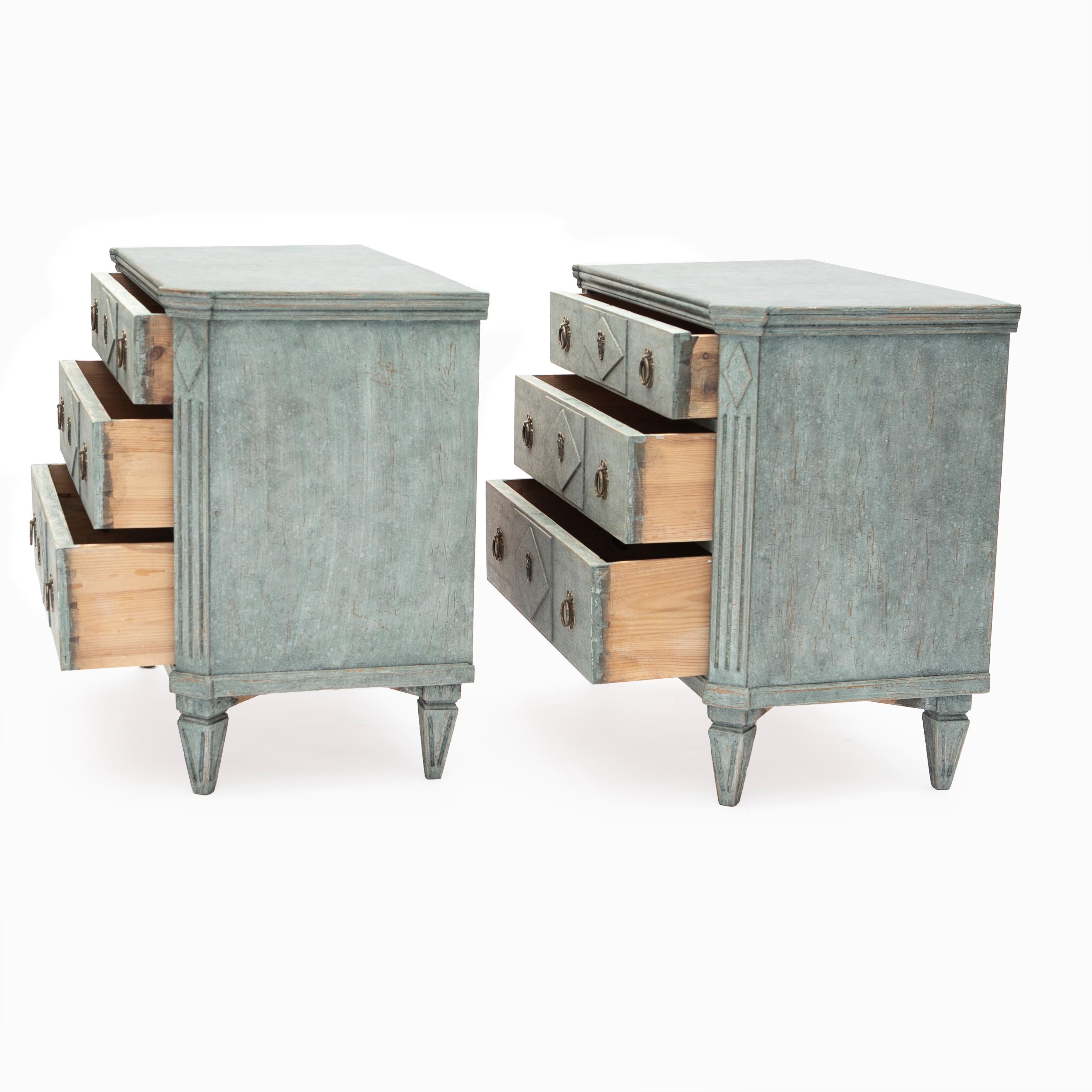 A pair of Swedish Gustavian style breakfront chest of three drawers, dating from the 19th century, painted in a light blue-green color scheme.

Each chest features a top with canted corners sitting above a front with three break drawers adorned
