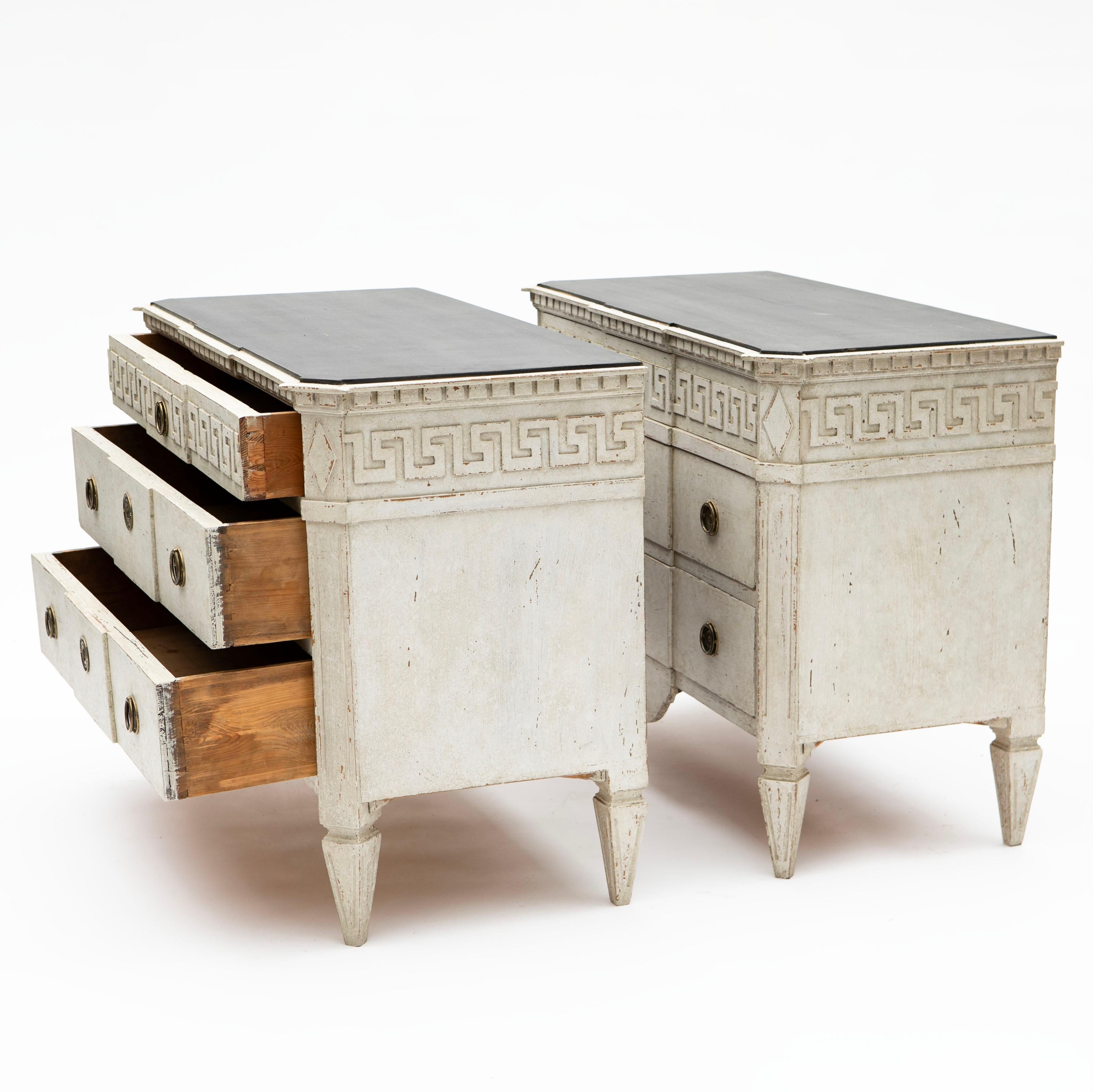 A pair of antique Swedish Gustavian style light-grey painted chest of three drawers, dating from the 19th century.
Each chest features a black painted rectangular top with canted corners in the front, sitting above a delicate meander décor molding