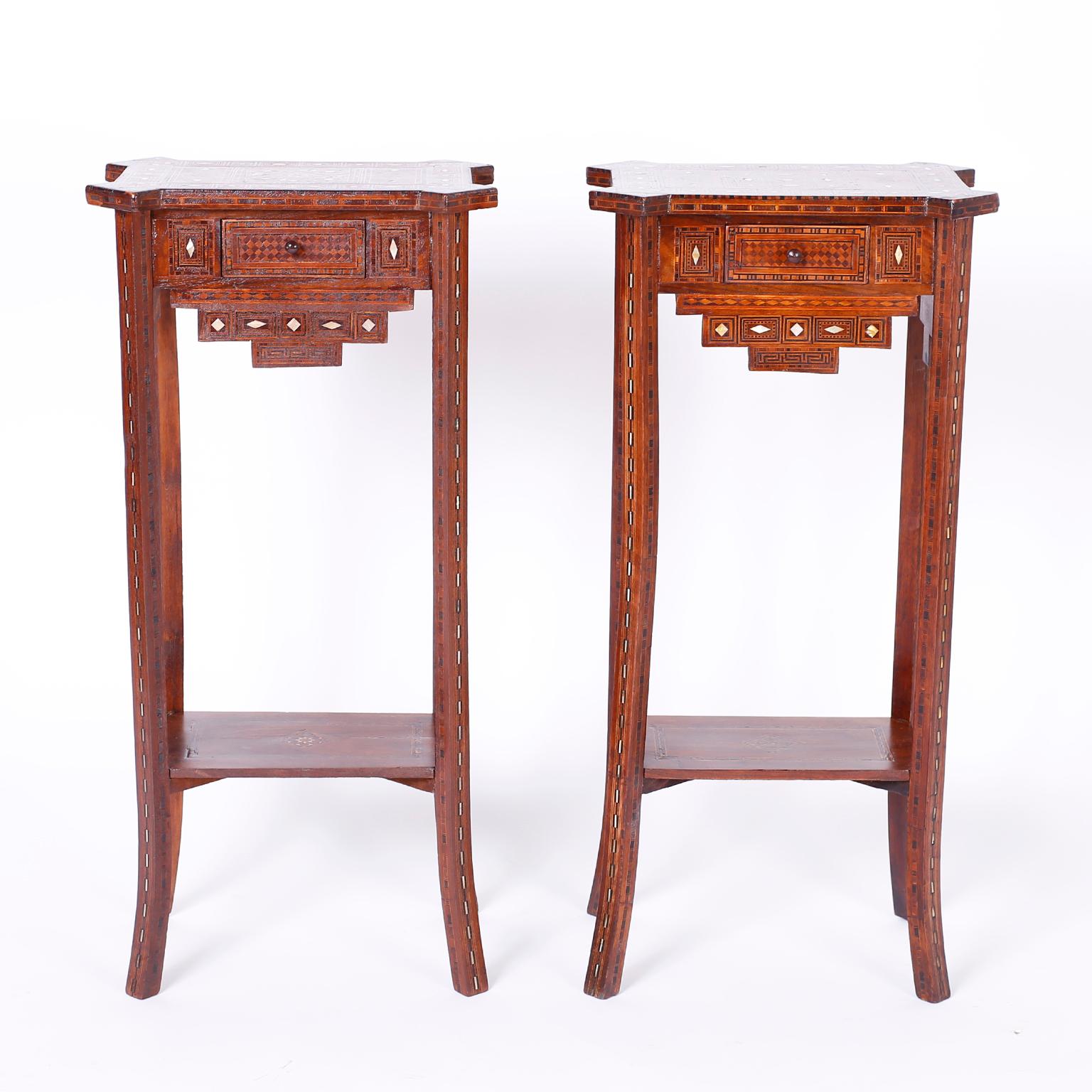 Refined pair of Syrian one drawer tables or stands with a tall, elegant form crafted in walnut and inlaid from top to bottom with geometric designs using mother of pearl, mahogany, ebony, and king wood featuring splayed legs and a desirable slim