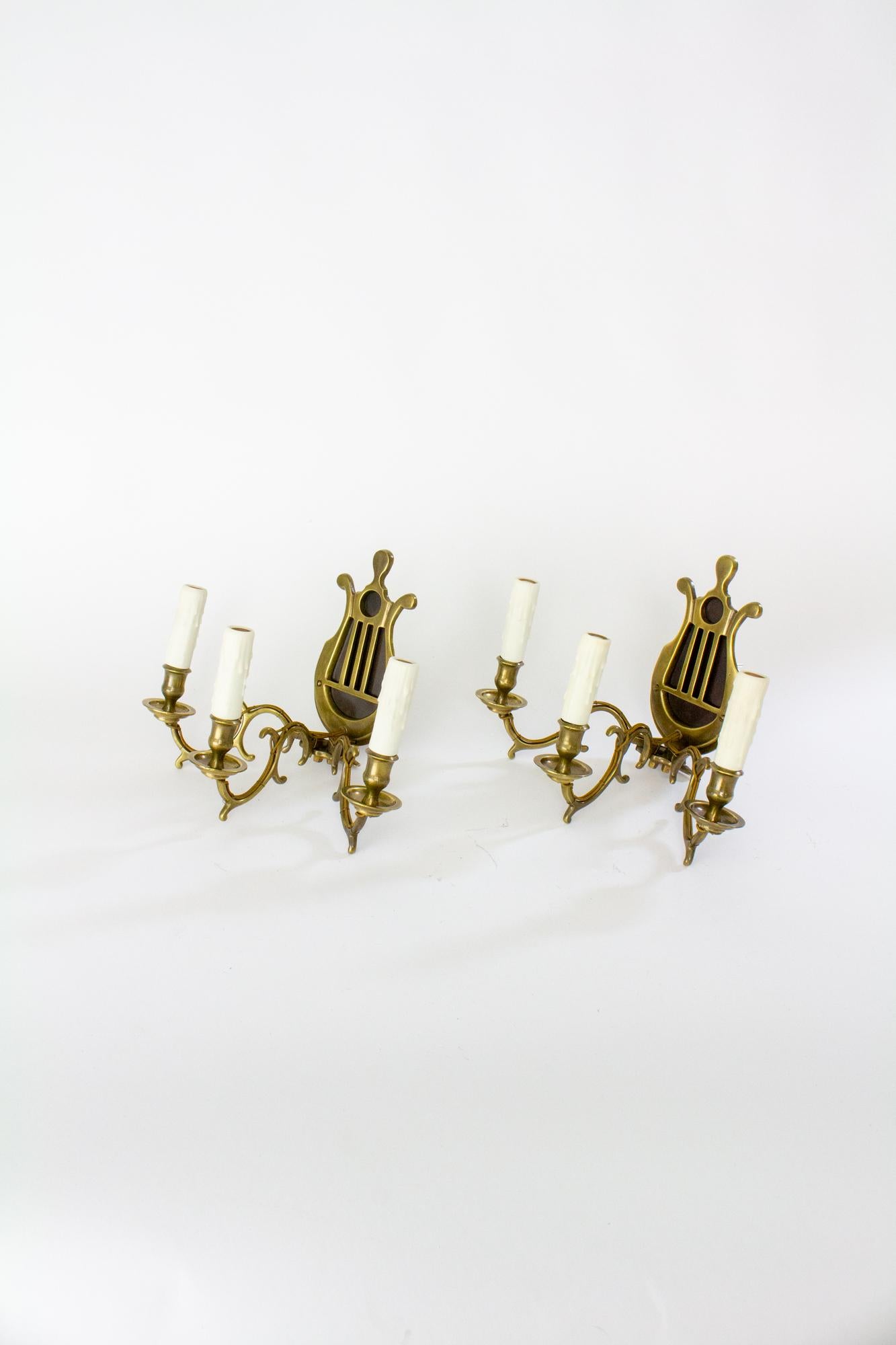 A pair of antique three arm lyre back sconces. Originally made for use with candles, these sconces have been carefully electrified. The arms have exterior wiring, with a very low profile. New polybeeswax candle covers with realistic drips. The