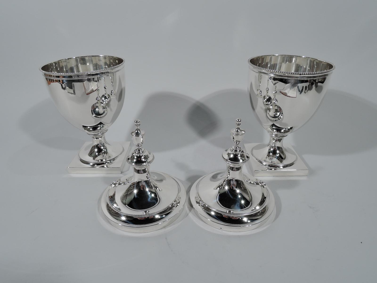Pair of Federal-style sterling silver covered urns. Made by Tiffany & Co. in New York, circa 1917.
Each: Ovoid bowl on raised foot mounted to square base. Double domed cover. Beading. An austere and self-referencing design with covered urn finial