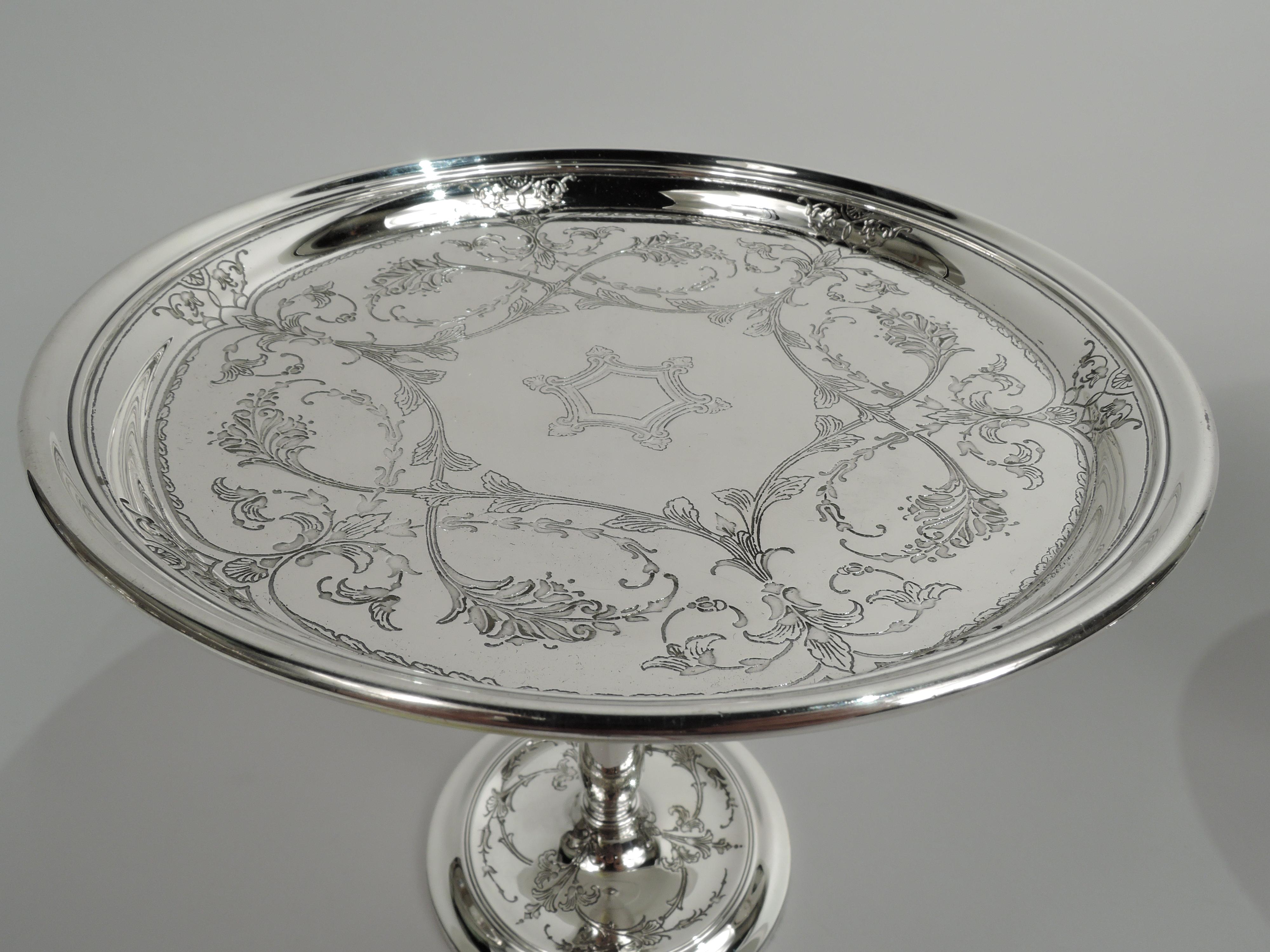 Pair of Tiffany Edwardian Classical sterling silver compotes. Made by Tiffany & Co. in New York, ca 1920. Each: Round and shallow bowl on upward tapering stem mounted to found foot with concave center. Entwined leafing scrollwork on well and foot.
