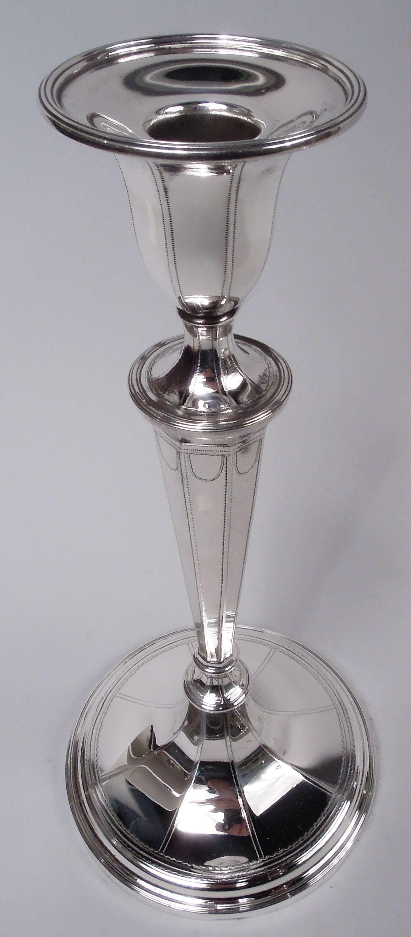 Pair of English Neoclassical-style sterling silver candlesticks. Made by Tiffany & Co. in New York, ca 1917. Each: Urn socket mounted to tapering shaft on raised and round foot. Pointillé frames and Vitruvian scroll borders. Faceted. Fully marked