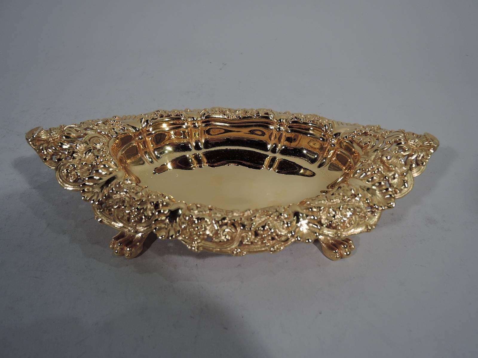 Pair of gilt sterling silver footed bowls. Made by Tiffany & Co. in New York, circa 1884. Each: Panelled ovalish well and scrolled and pierced turned-down rim with flowers, berries, and leaves. Rests on four foliate-scroll mounted paws. Substantial