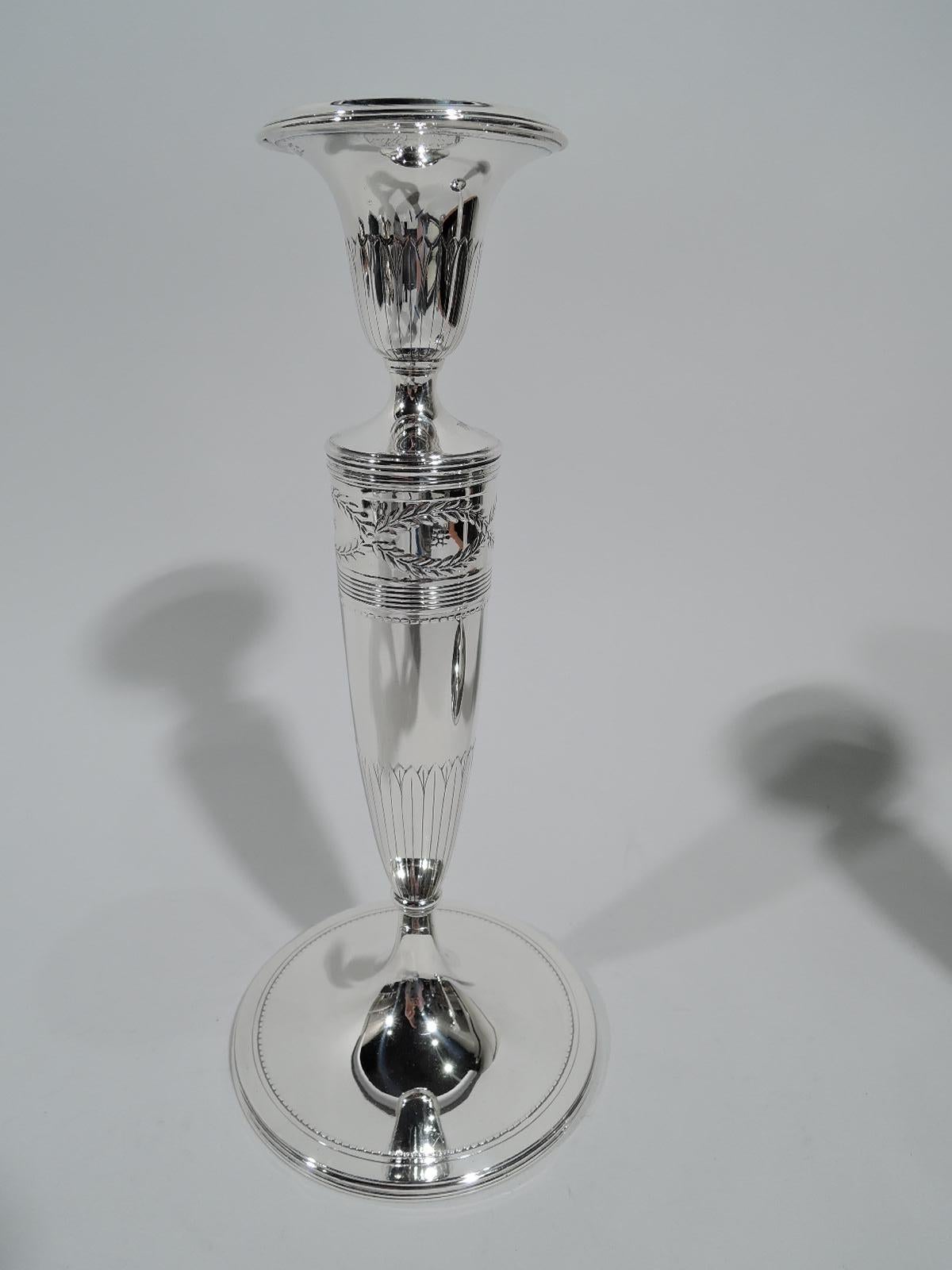 Pair of Winthrop sterling silver candlesticks. Made by Tiffany & Co. in New York, circa 1911. Each: Tapering columnar shaft on raised foot. Urn socket with detachable bobeche. Shaft top has the classic laurel-wreath border inset with flower heads.