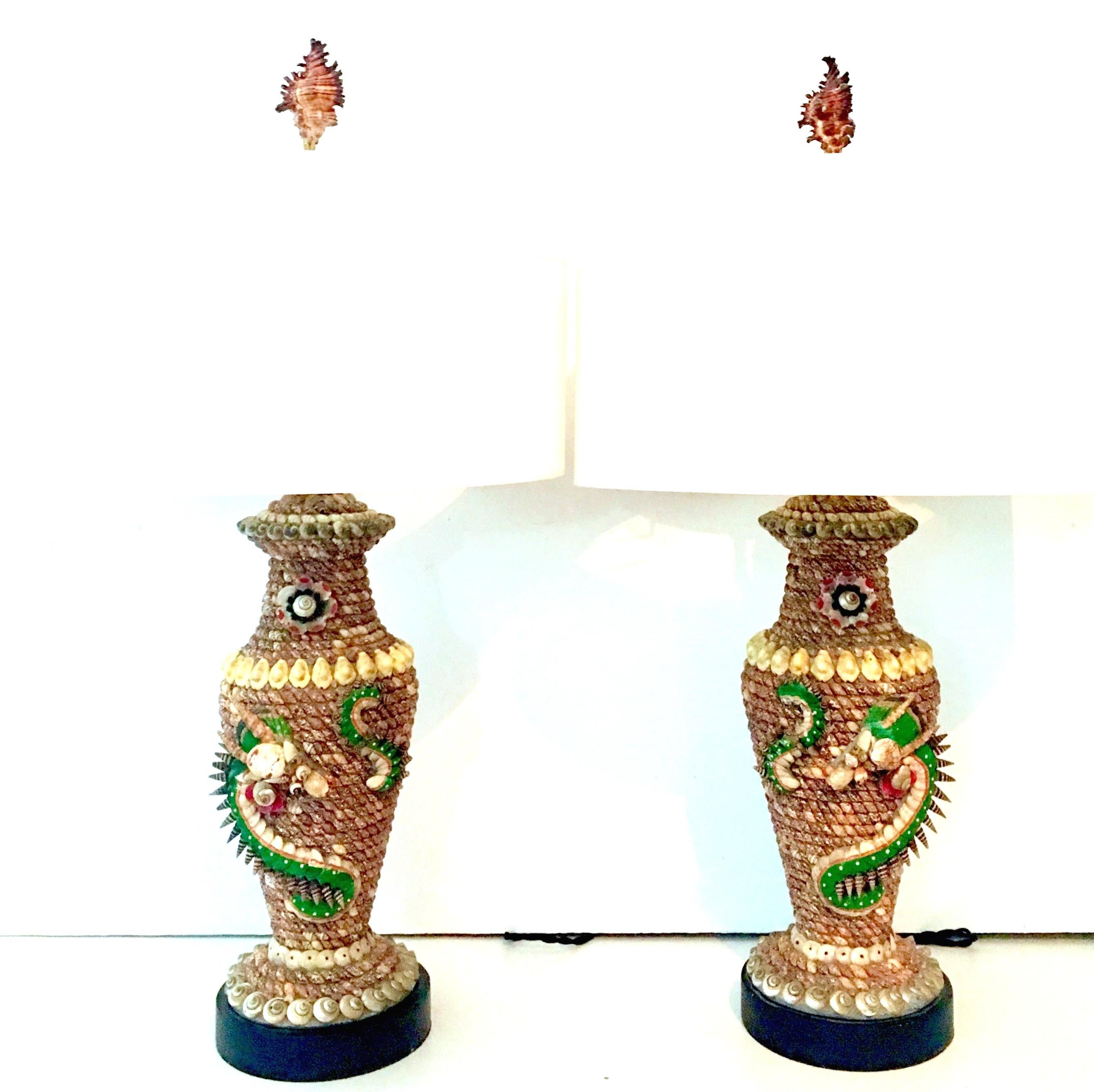 Pair Of Rare Mid-20th Century Tony Duquette style finely hand crafted seashell encrusted dragon motif high relief table lamps. These hand crafted table lamps feature miniature sea shells in a variety of colors, painstakingly hand applied with a high