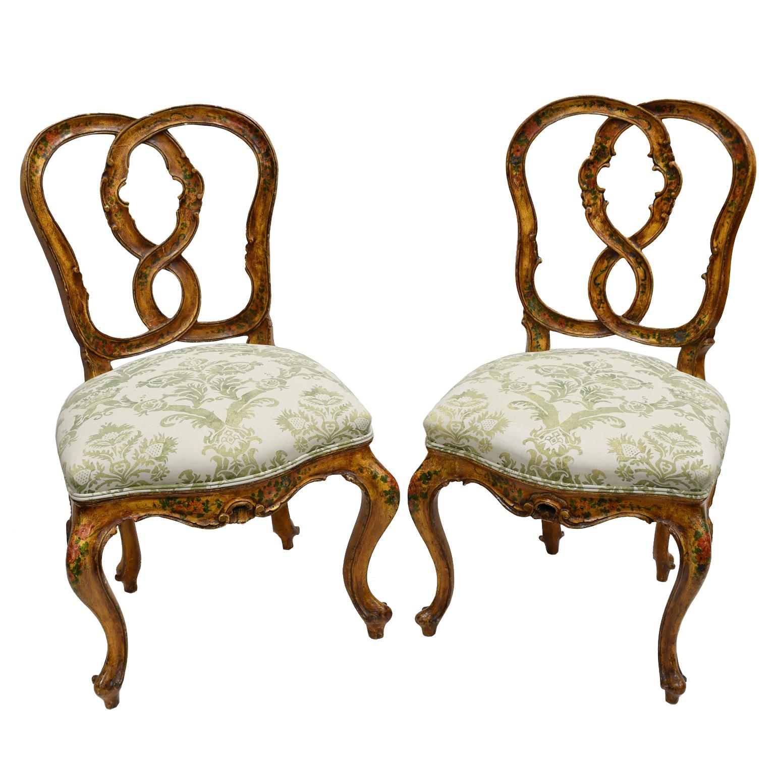 A charming pair of Venetian his & hers dining chairs with one chair being slightly larger than the other. Wooden frames have a glazed yellow-ochre paint with hand-painted flowers and feature figure eight backs, cabriole legs and upholstered seats.