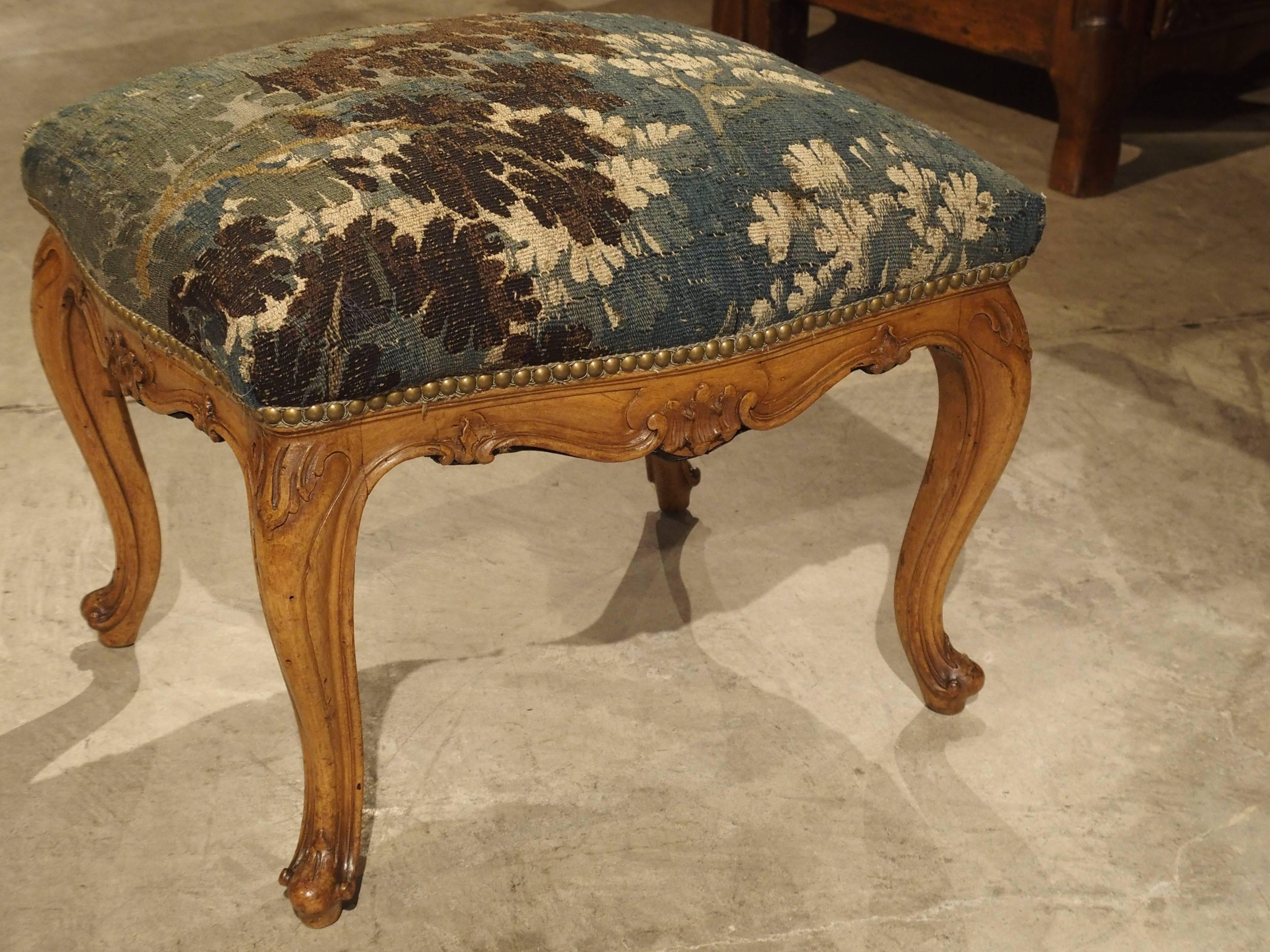 This elegant pair of Venetian walnut wood stools dates to the 19th century (tapestry is 18th century). The carving of these stools is very fine and has a variety of foliate motifs. There are double C and S scroll linear moldings, while graceful