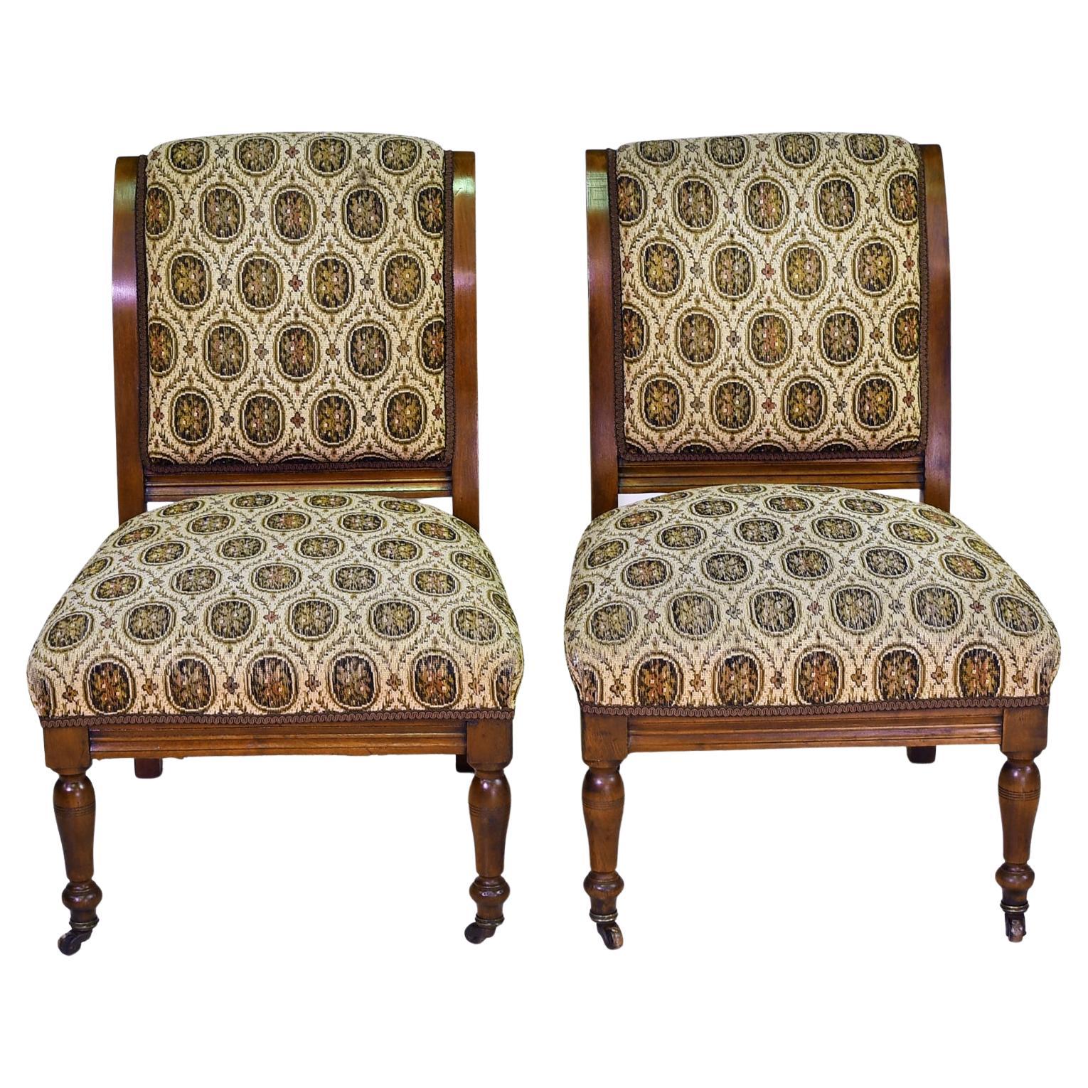 A pair of early American Victorian slipper chairs in walnut with upholstered back & seat, circa 1840. Features an outward scrolled back, carved seat rail & turned front legs. Original upholstered framework has springs, designed for added comfort.