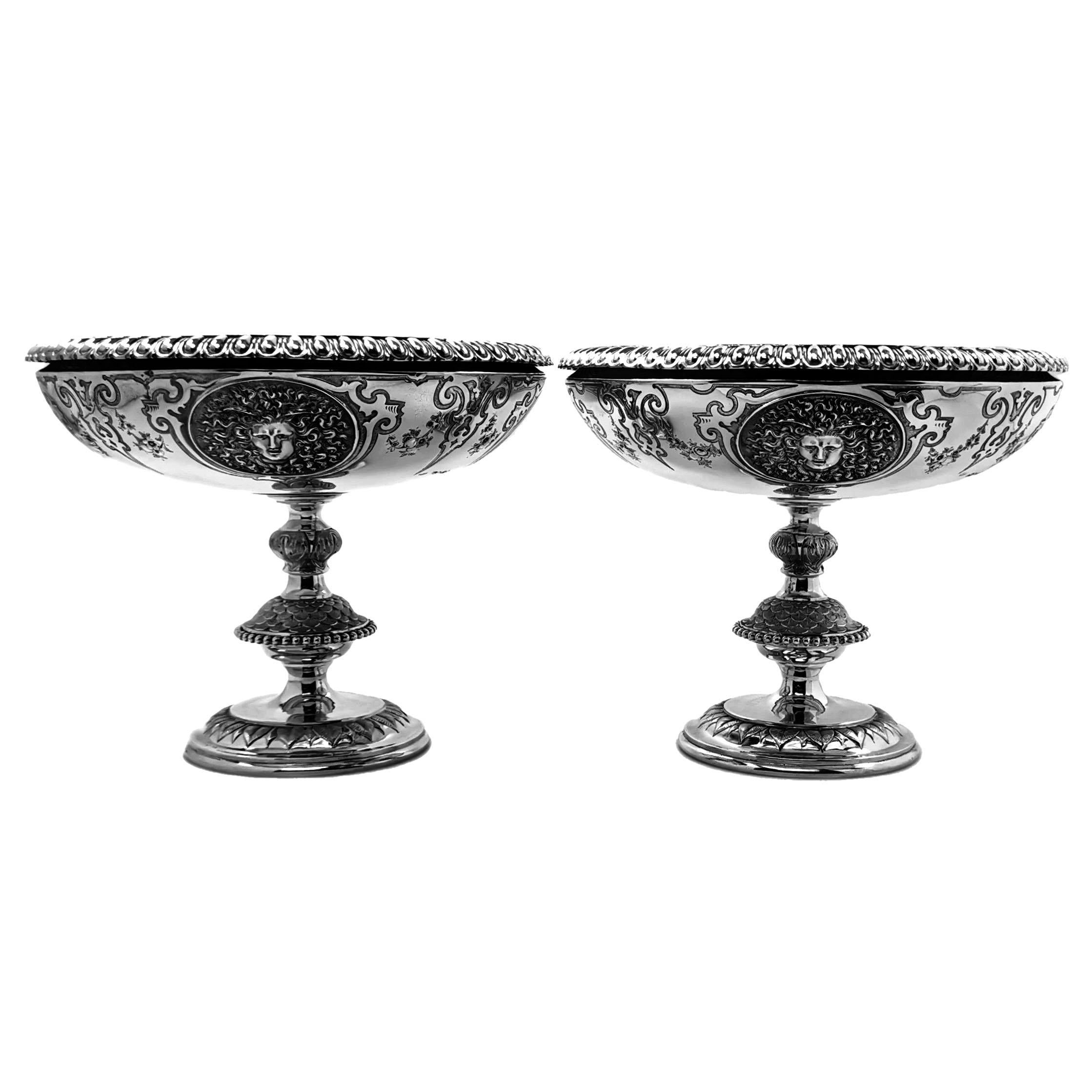 A pair of impressive Antique Solid Silver Comports standing impressive ornate knopped columns. The Bowls of the Comports have a pair of blank cartouches alternating with a pair of beautifully chased classical faces. The spread foot and column of