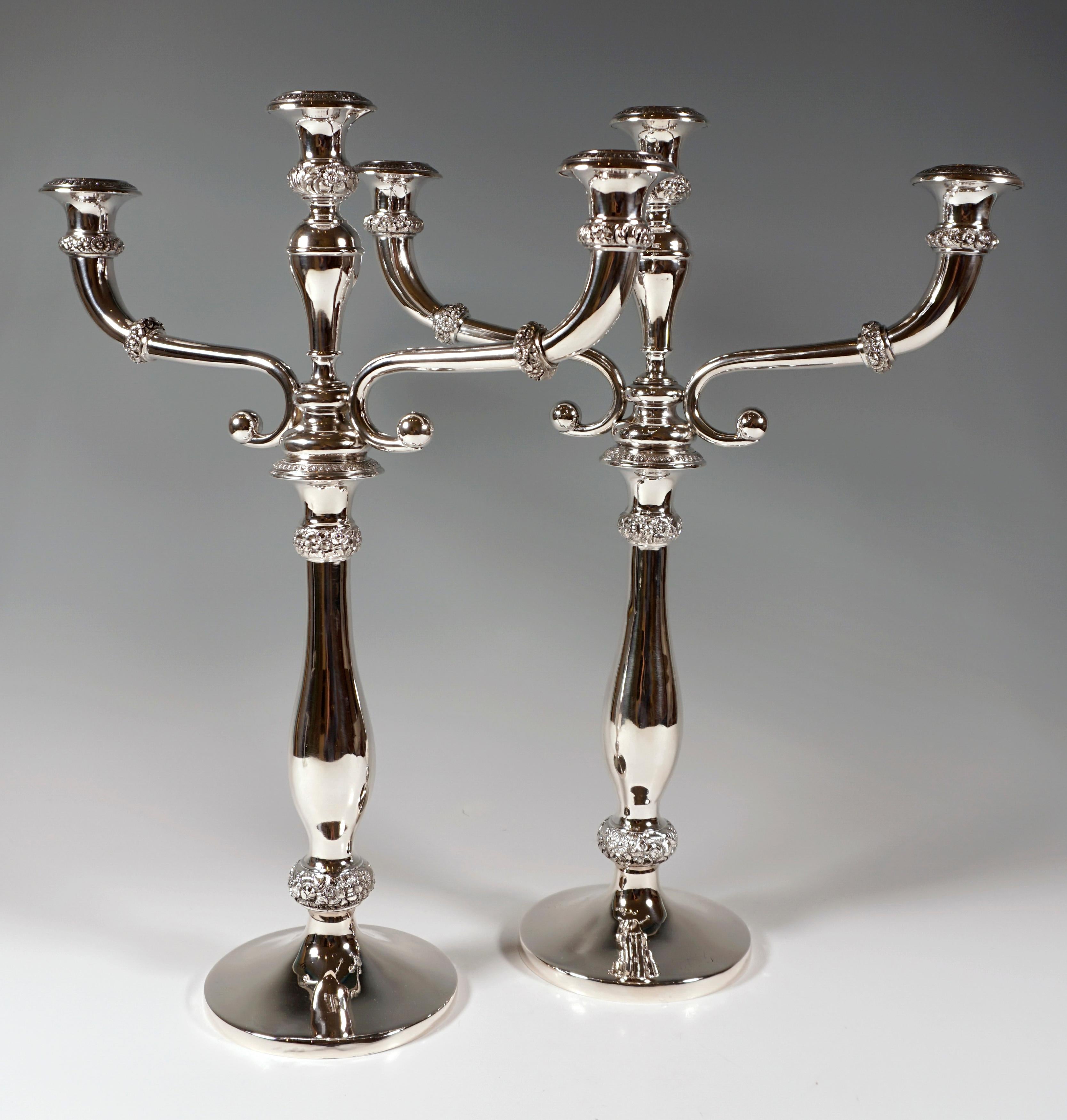 Two elegant silver candleholders on round stand with smooth baluster shaped stem, beaded rings decorated with sculptural floral & rocaille decor, vase shaped spouts with chased palmette decor on the high arched eaves pieces, can be used as single