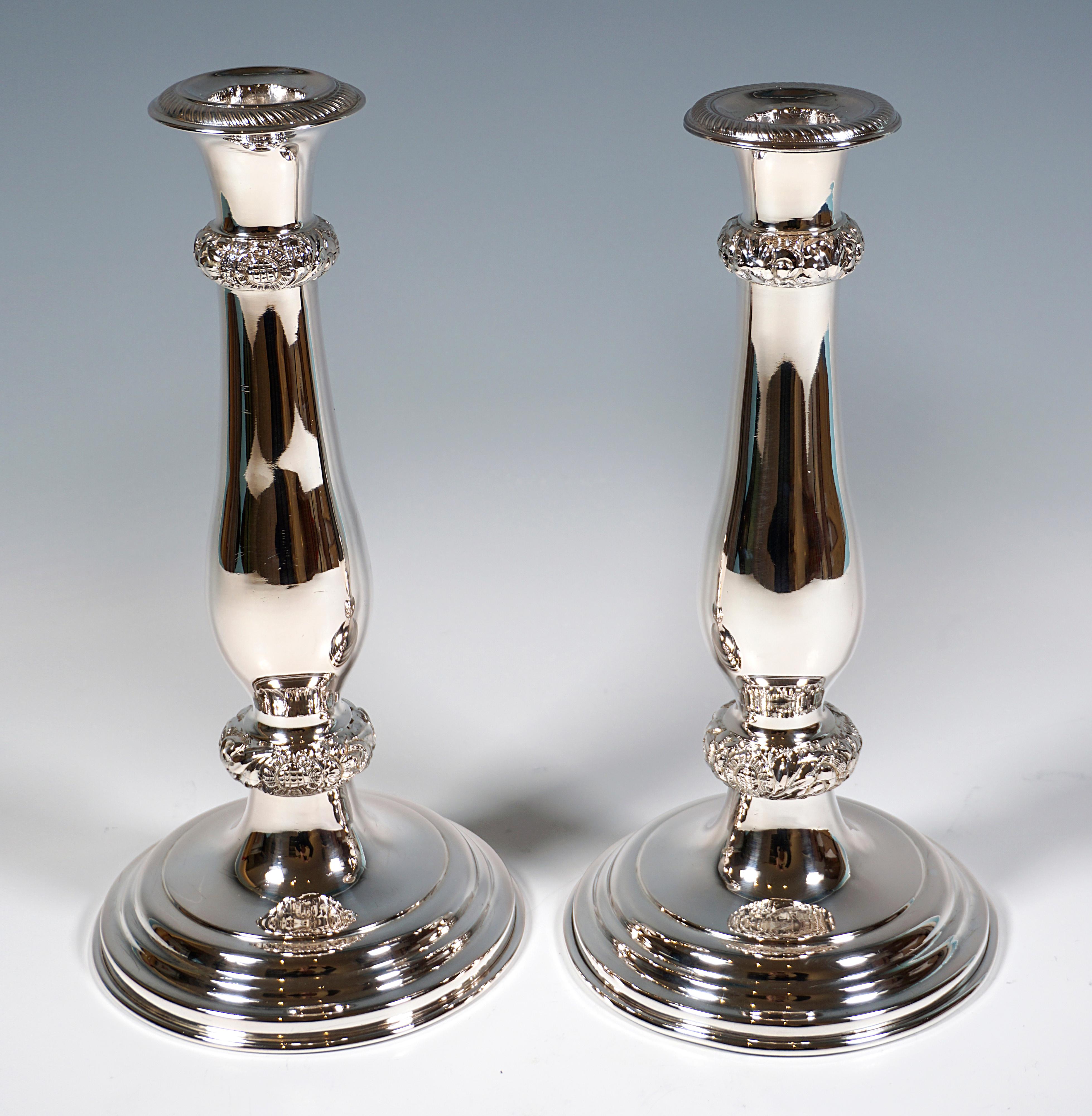 Deux chandeliers festifs en argent Biedermeier sur un pied rond en forme de dôme à gradins avec une tige lisse en forme de balustre, des anneaux perlés décorés de fleurs et de Rocaille en relief, des becs en forme de vase avec un ruban en cordon en