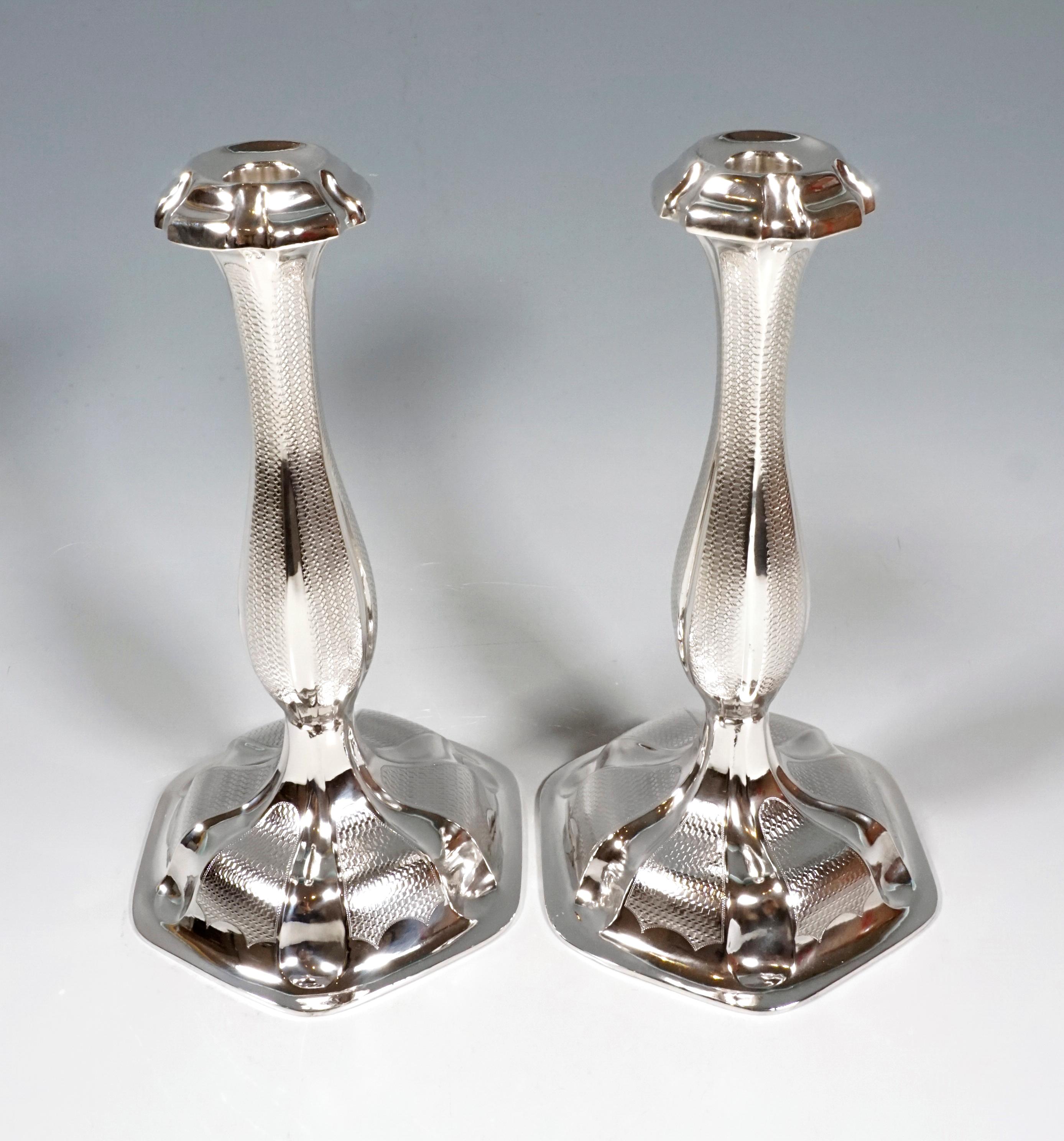 Pair of silver candle holders on a six-pointed, cambered base with guilloche decoration. Curved shaft, engine-turned, with a slightly flared, vase-shaped spout with a six-pointed rosette.

Branded by the Wheel mark, Austrian official hallmark: 13