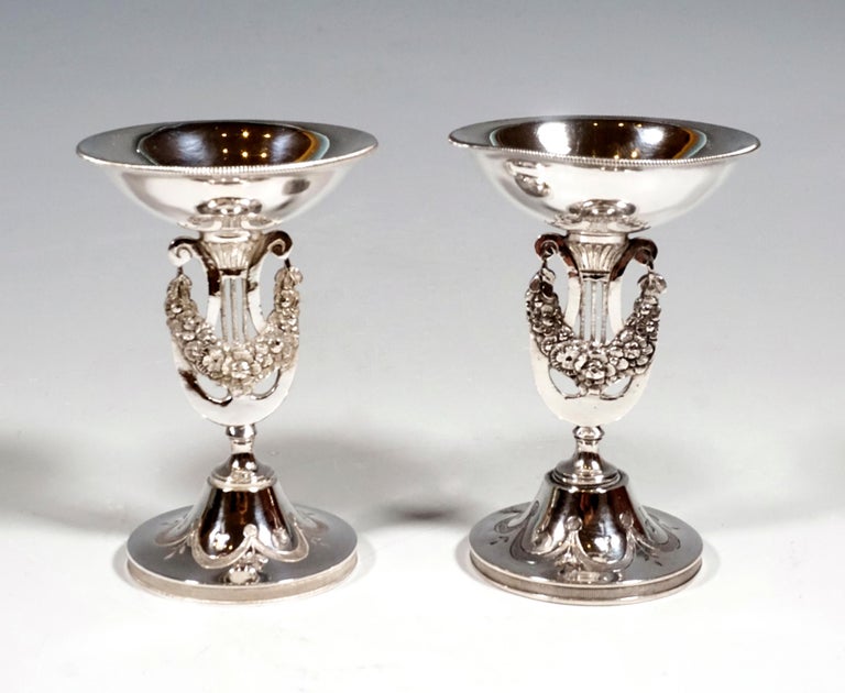 Two tall silver spice bowls on a round base with guilloche ribbon decoration, stem in the form of a cut-out lyre with a flower garland, above a smooth bowl with a slightly flared mouth rim worked out as a cord ribbon.

Finest handwork by the