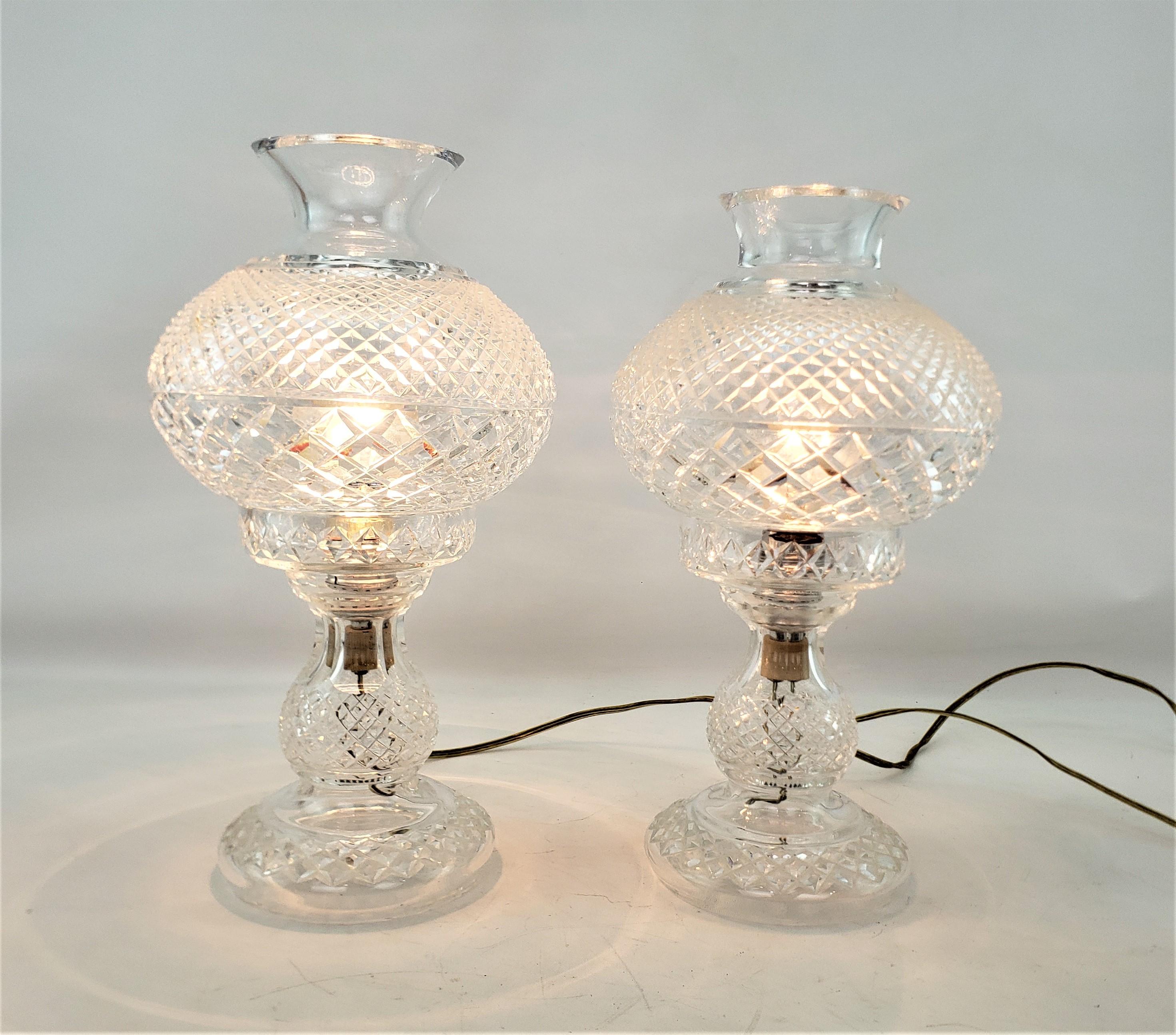 This pair of antique lamps were made by the renowned Waterford company of Ireland in approximately 1920 and done in a period style. The lamps are composed of cut crystal with a diamond pattern on both the shade and base. These hurricane styled lamps