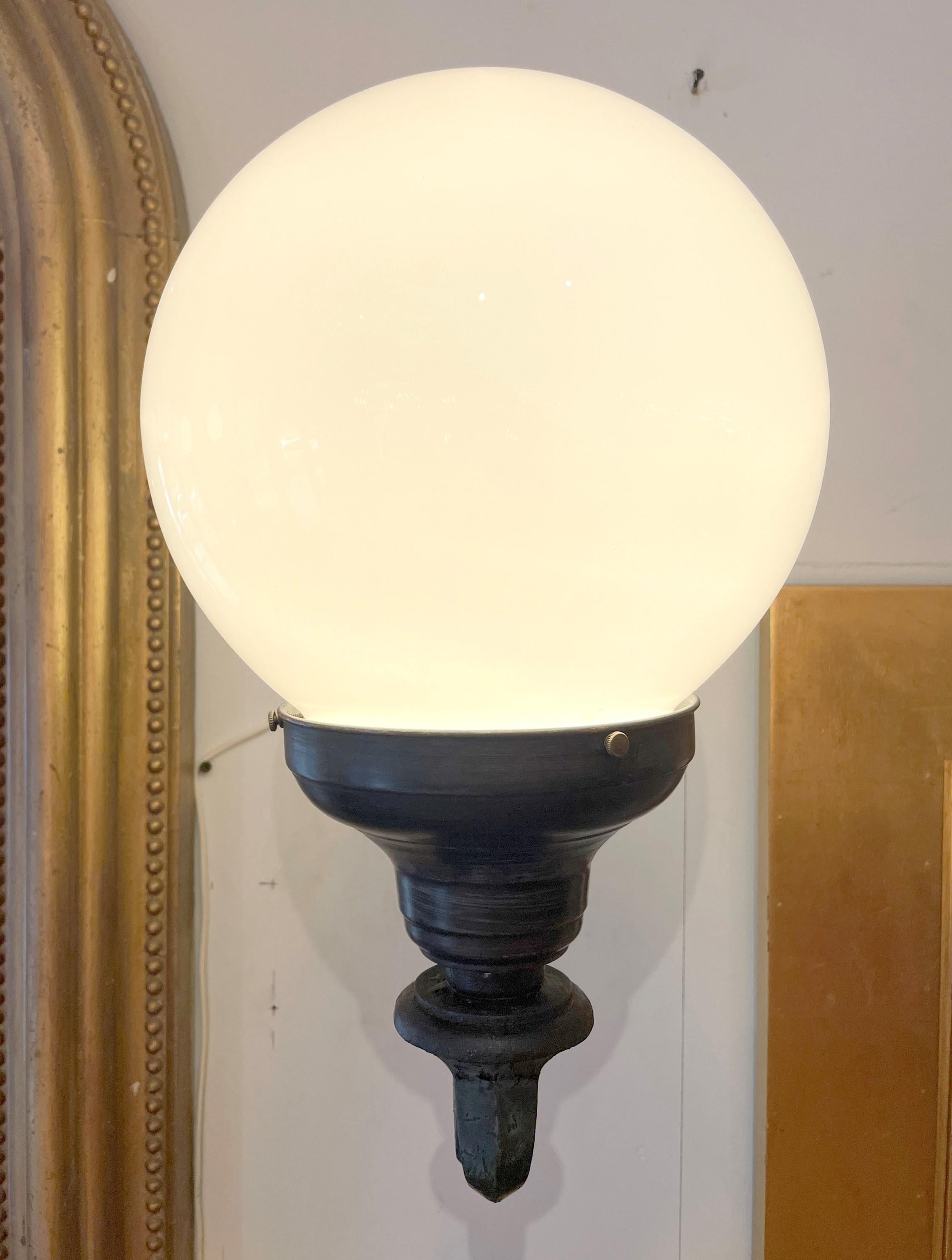 Early 20th century pair of exterior building sconces. Made with a cast iron body and brass shade holders. These also feature white ball globe shades. Cleaned and restored. Priced as a pair. Please note, this item is located in one of our NYC