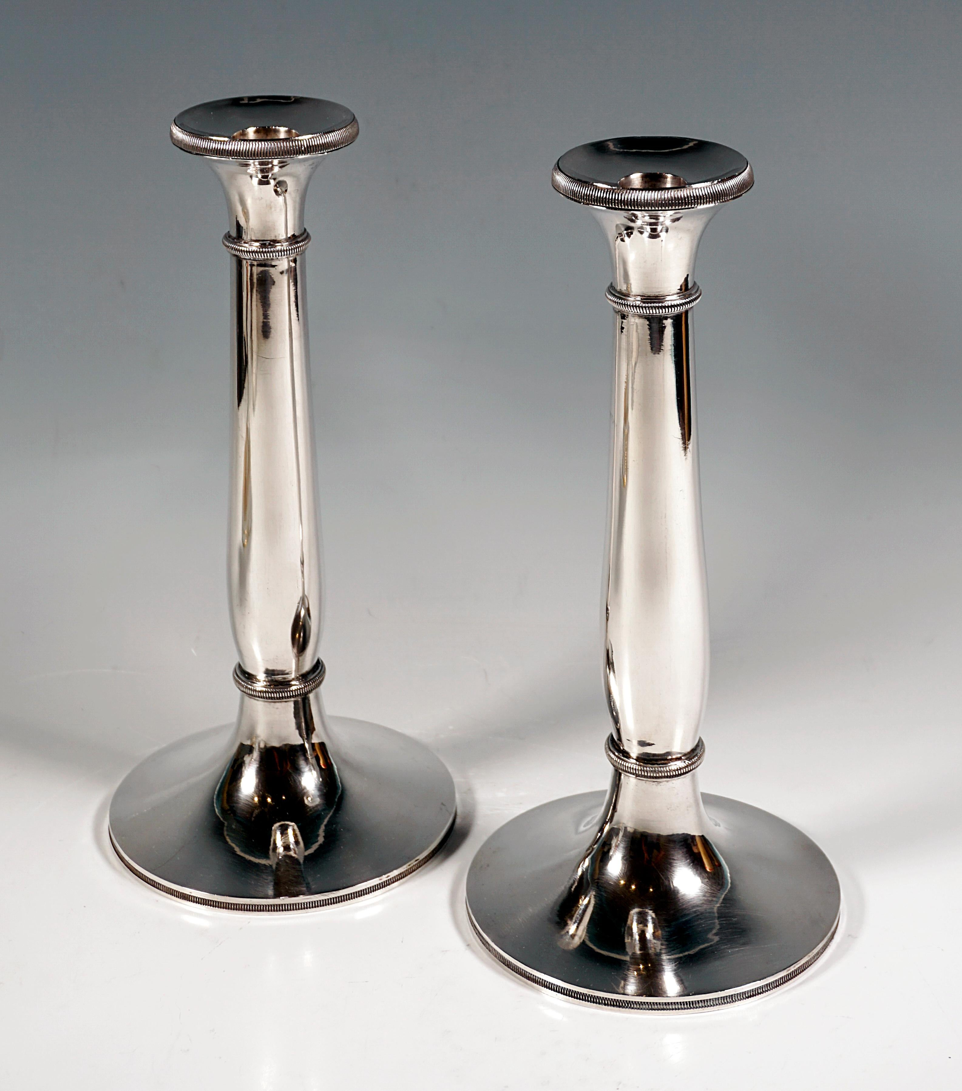 Zwei elegante, schlichte frühe Biedermeier-Kerzenhalter aus Silber auf rundem Ständer mit leicht geschwungenem, glattem Schaft, getriebenem Dekor am Rand des Fußes, an den schmalen Wulstringen und am oberen Rand der leicht ausgestellten