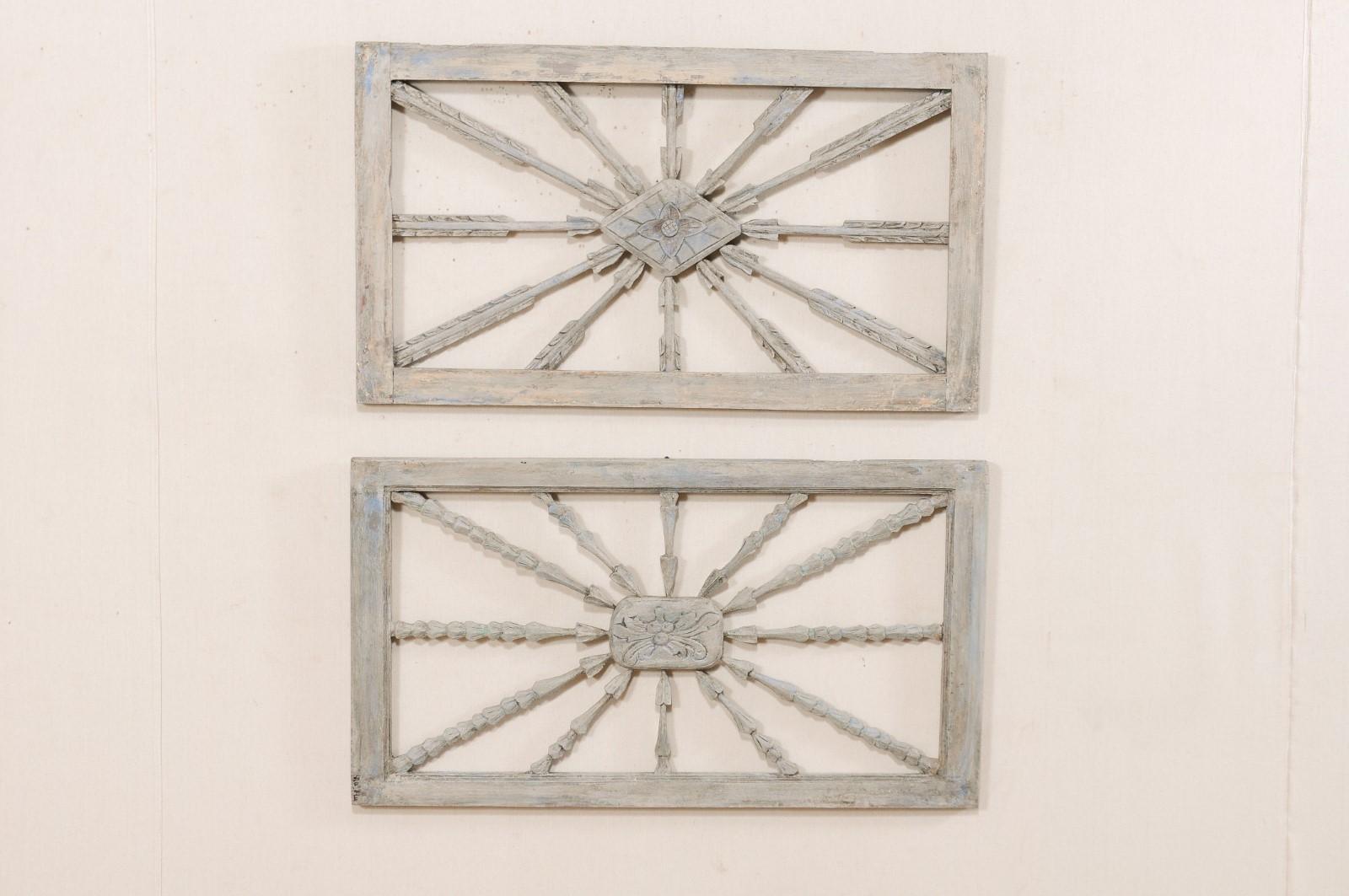 A near-pair of carved and painted wood window transoms from the early 20th century. This pair of antique window transoms have a clean, rectangular shaped surround, with nice display of carved-wood arrows pointing inward along all sides, to a center