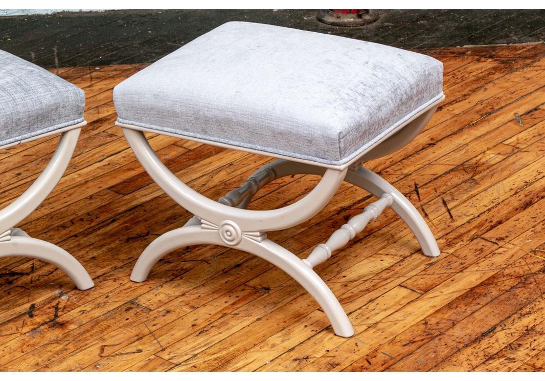 Fine diminutive footstool pair of neoclassical style footstools in custom lacquer and upholstery. Curved X forms with roundels in the centers and turned side stretchers. In custom pale gray lacquer and reupholstered in Savoy designer dusty pale blue