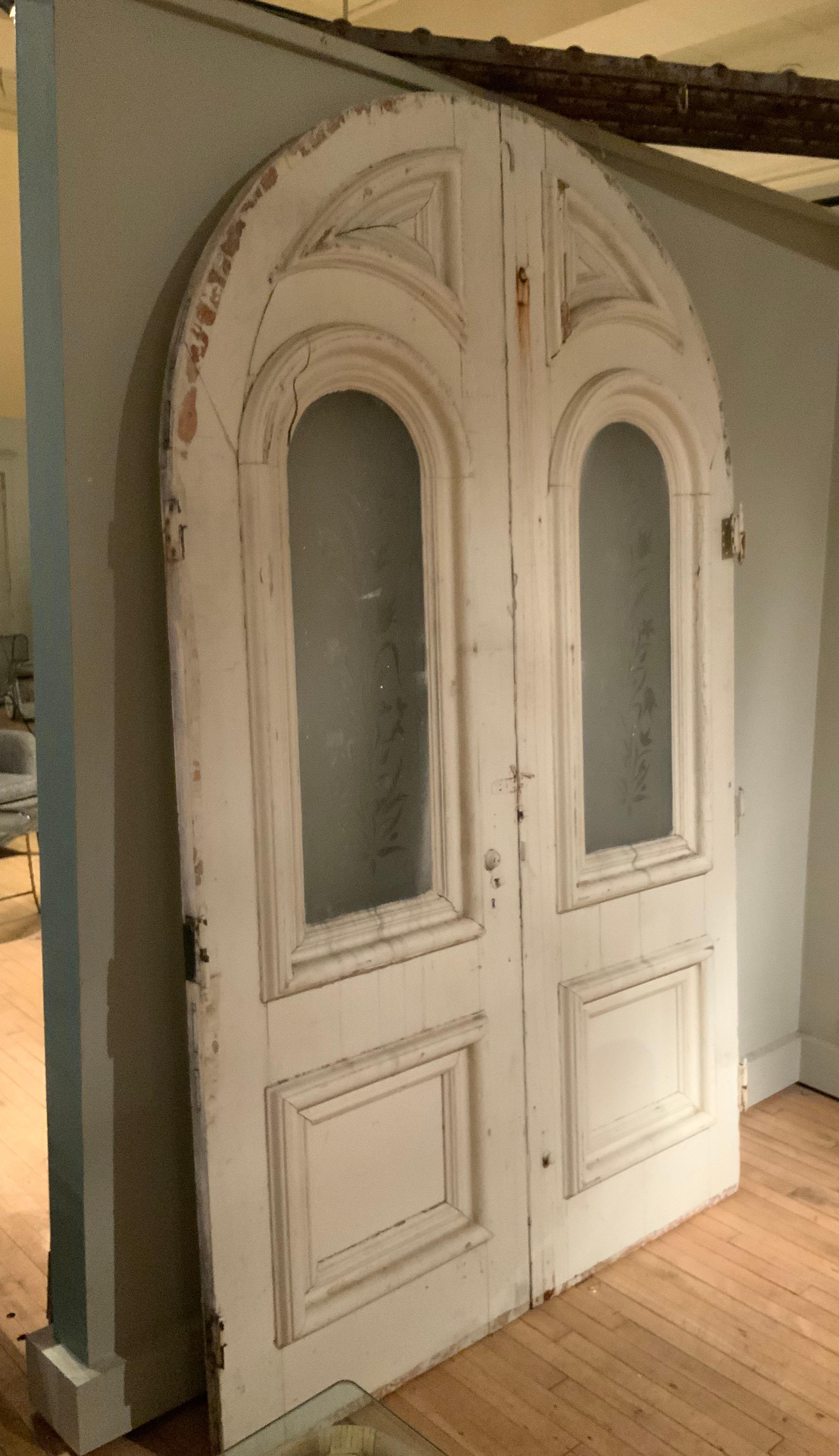 A very handsome pair of 1920's arch top exterior doors, beautifully made with elaborate paneled molding and containing the original arch top etched glass panels. these doors are in good structural condition, with age expected wear and one cut line