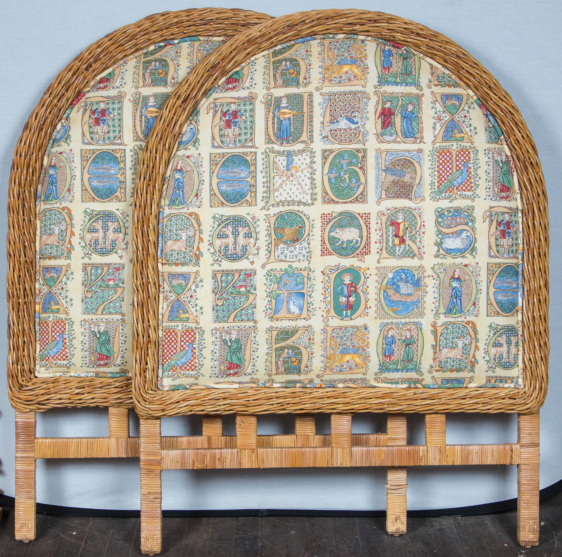 A pair of tall upholstered twin size headboards with thick woven wicker trim and rattan wrapped legs. Upholstery is in good condition. Renaissance style illustrated alphabet fabric.