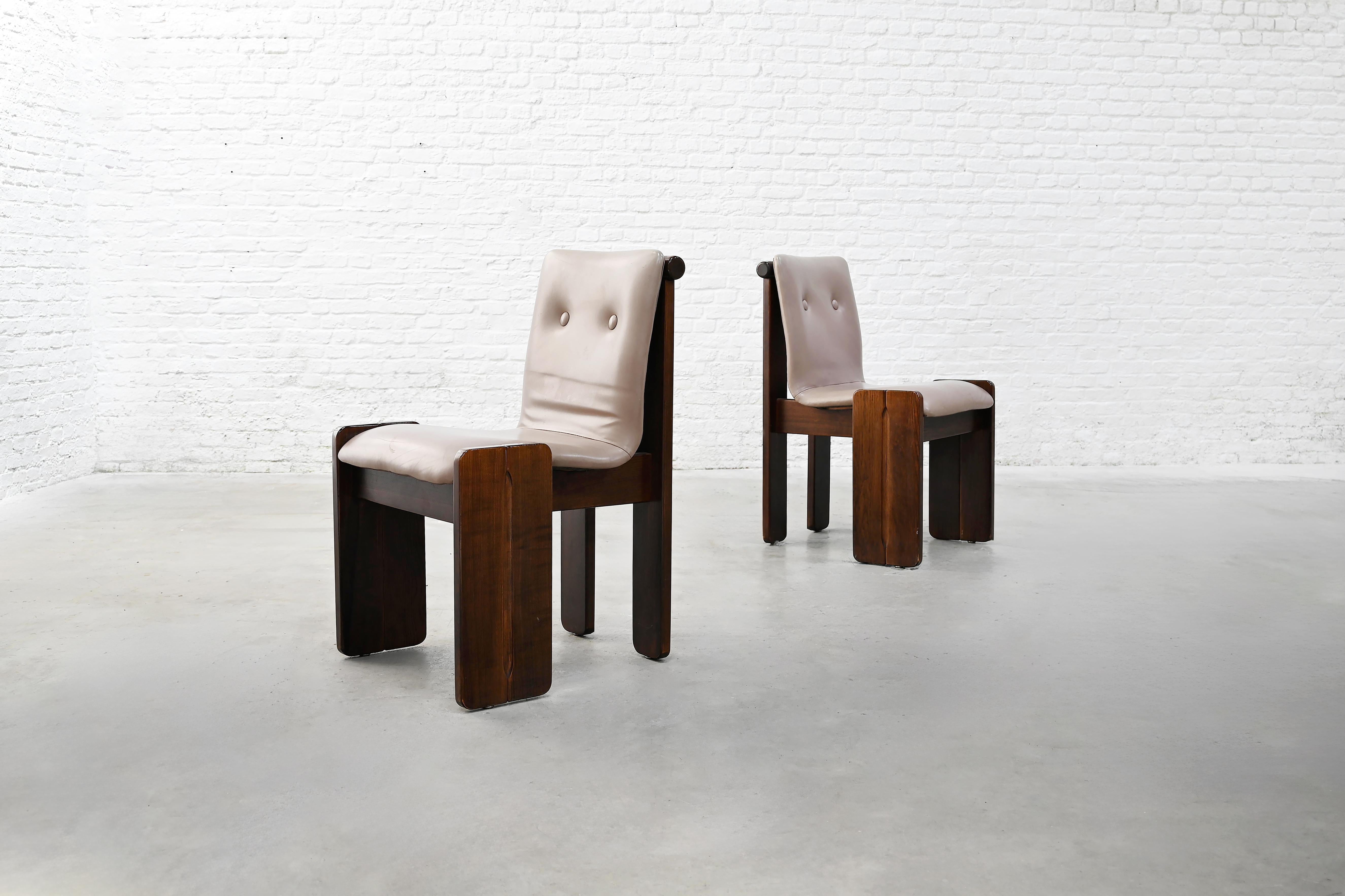 A pair of 1970s chairs with sculptural oak frames and a distinctly architectural character. The design is defined by its clean vertical lines, square-edged construction, and a subtle projection of the rear legs beyond the seat. The chairs feature