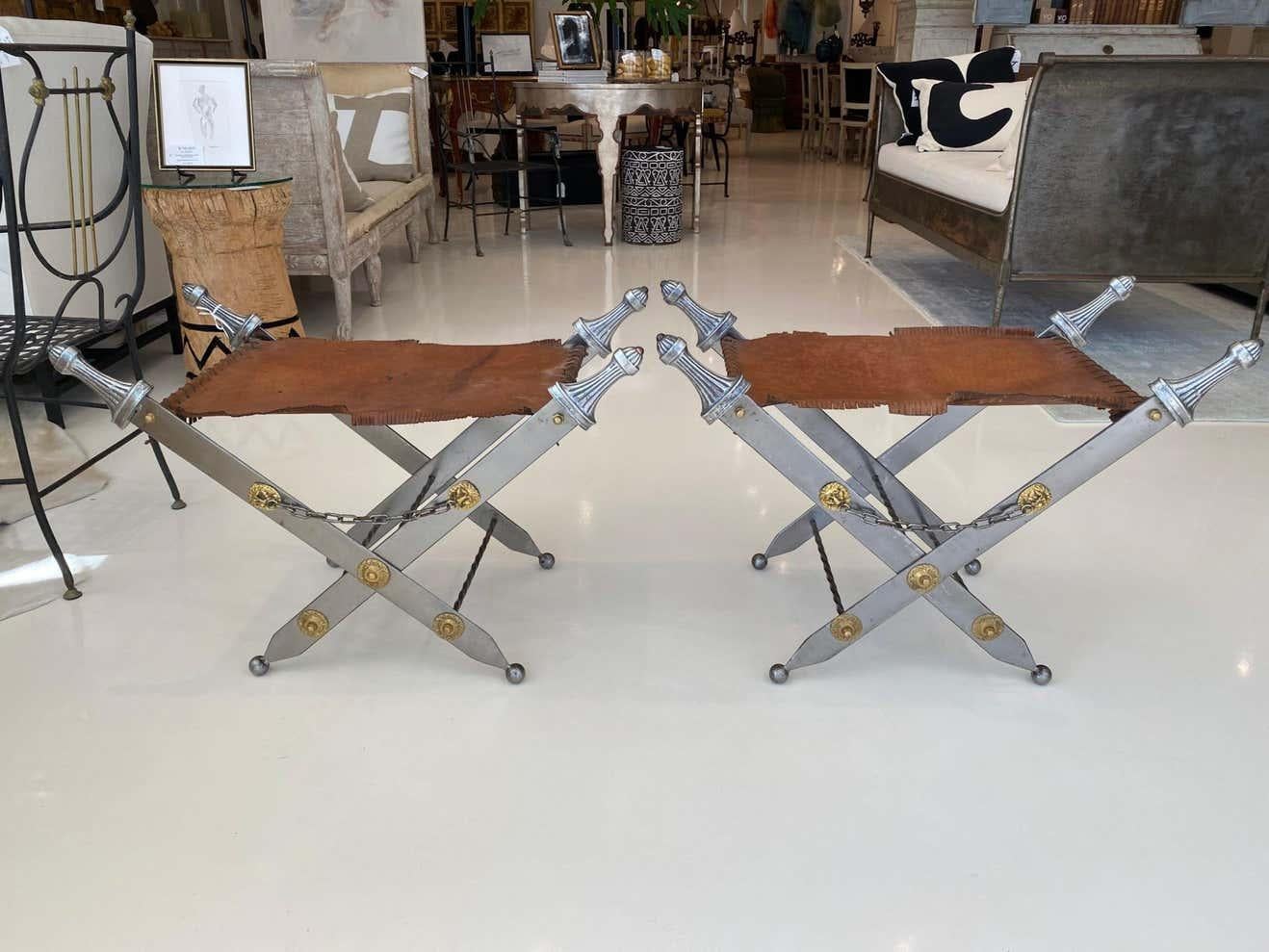 This is a pair of stools in fringed leather with metal sword frames. Brass accent lions and medallions are connected by a chain.. The stools have a Baronial vibe that adds to their charm. They are foldable and therefore have a very faint line in the