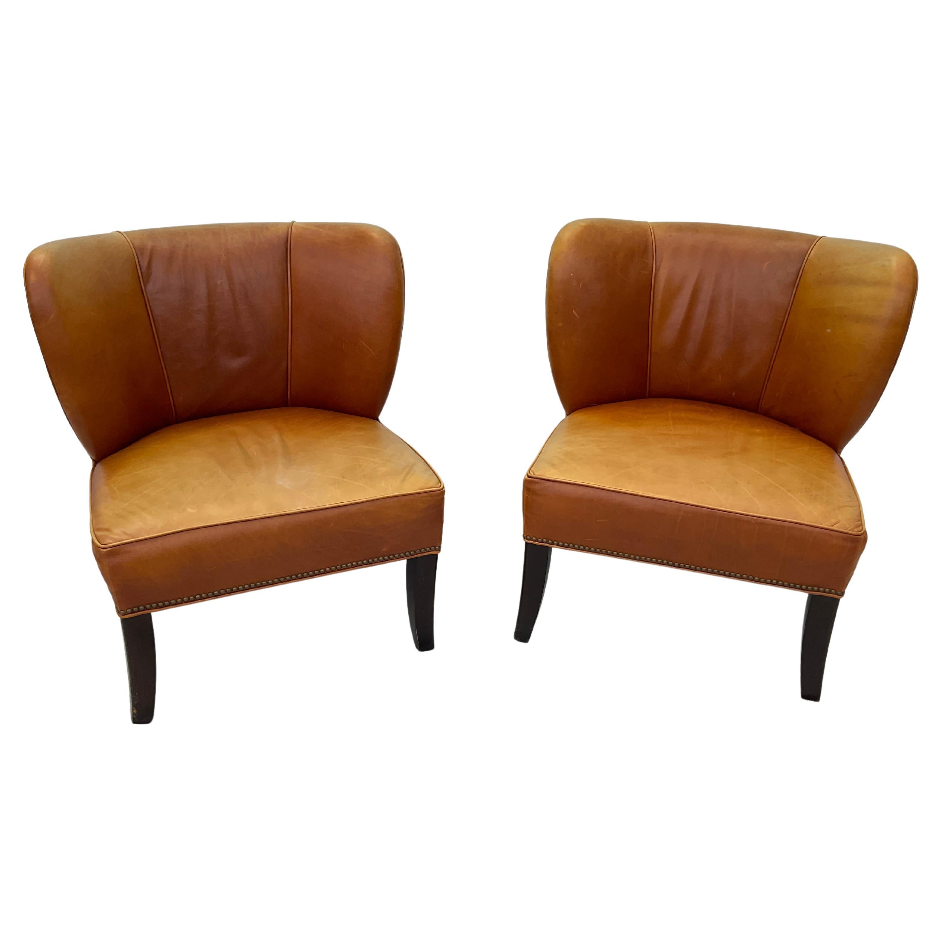Handsome pair of Arhaus Italian leather lounge chairs in a rich amber shade with brass nail head trim on ebonized wooden legs. Nice broken in leather in overall good condition. Top grain Italian leather, craftsman-built by artisans in North