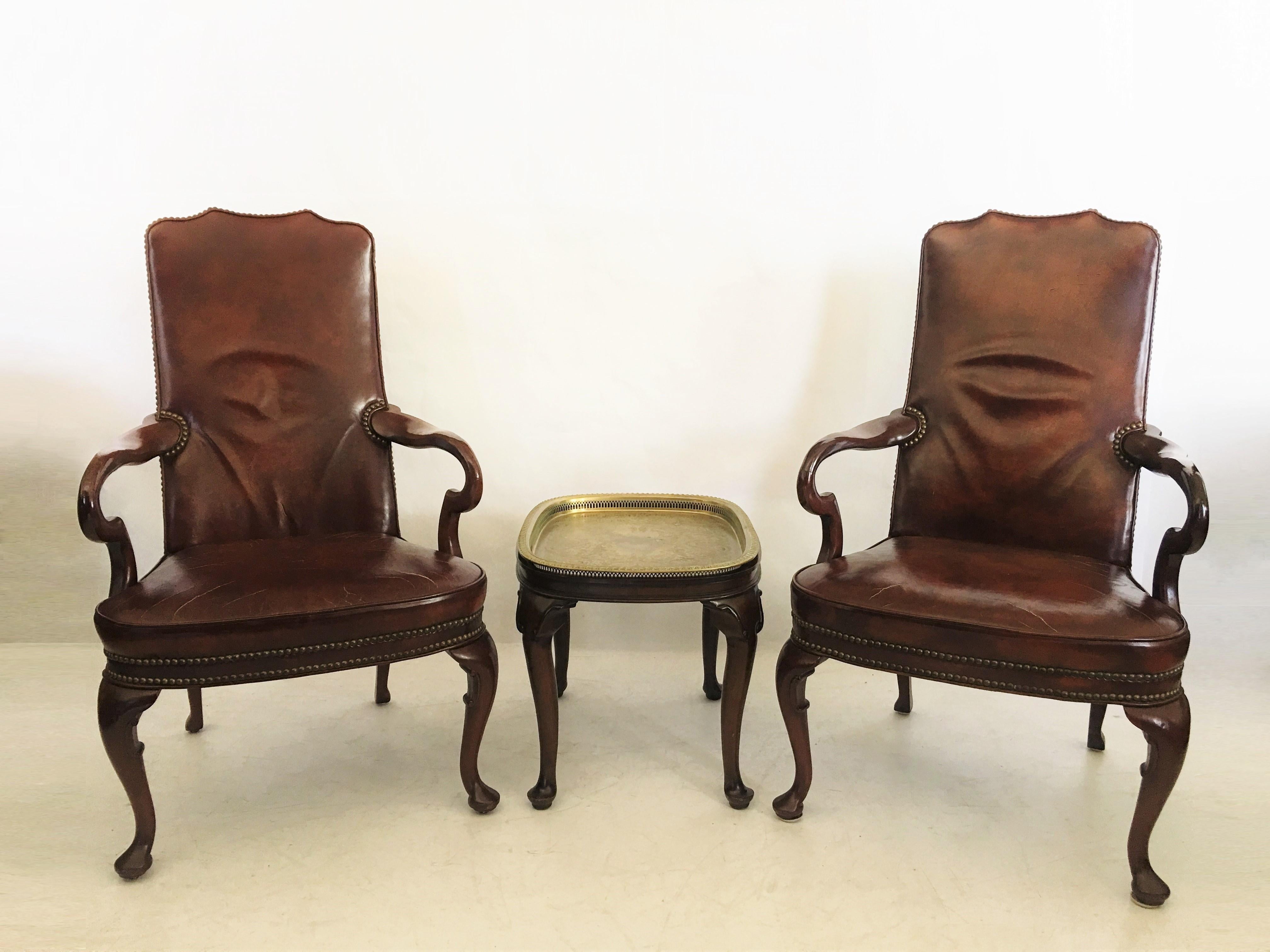 High quality and great workmanship pair of Queen Anne style armchairs by Hickory Chair Co. The mahogany-finished frames are upholstered in oxblood color with brass nail head trim. Each chair features a yoke crest above a padded back and seat flanked
