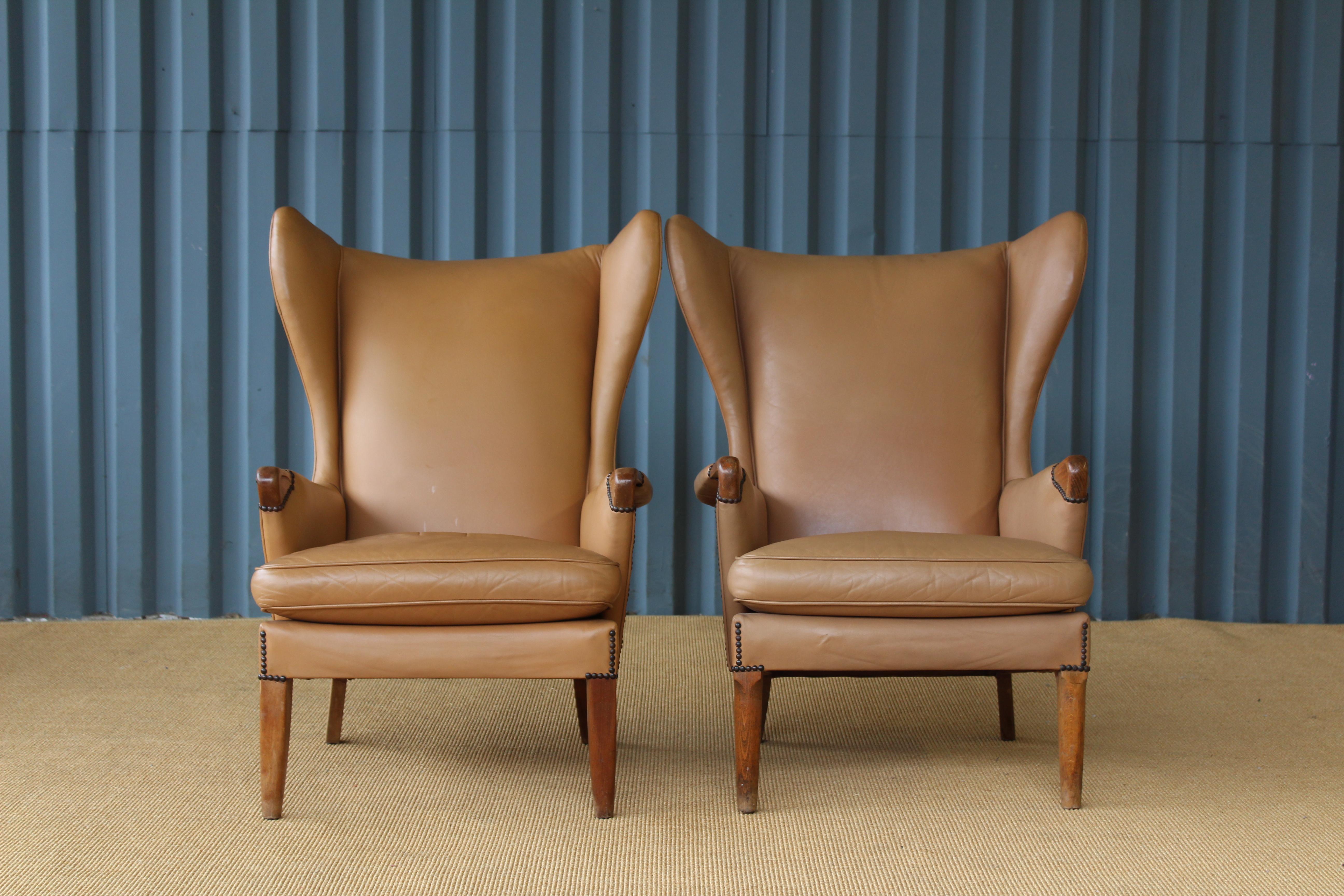 Pair of armchairs by Parker Knoll, 1950s, United Kingdom. They feature the original tan leather upholstery with brass nailhead details along the backside and near the legs. Leather is in very nice condition considering age with minimal signs of