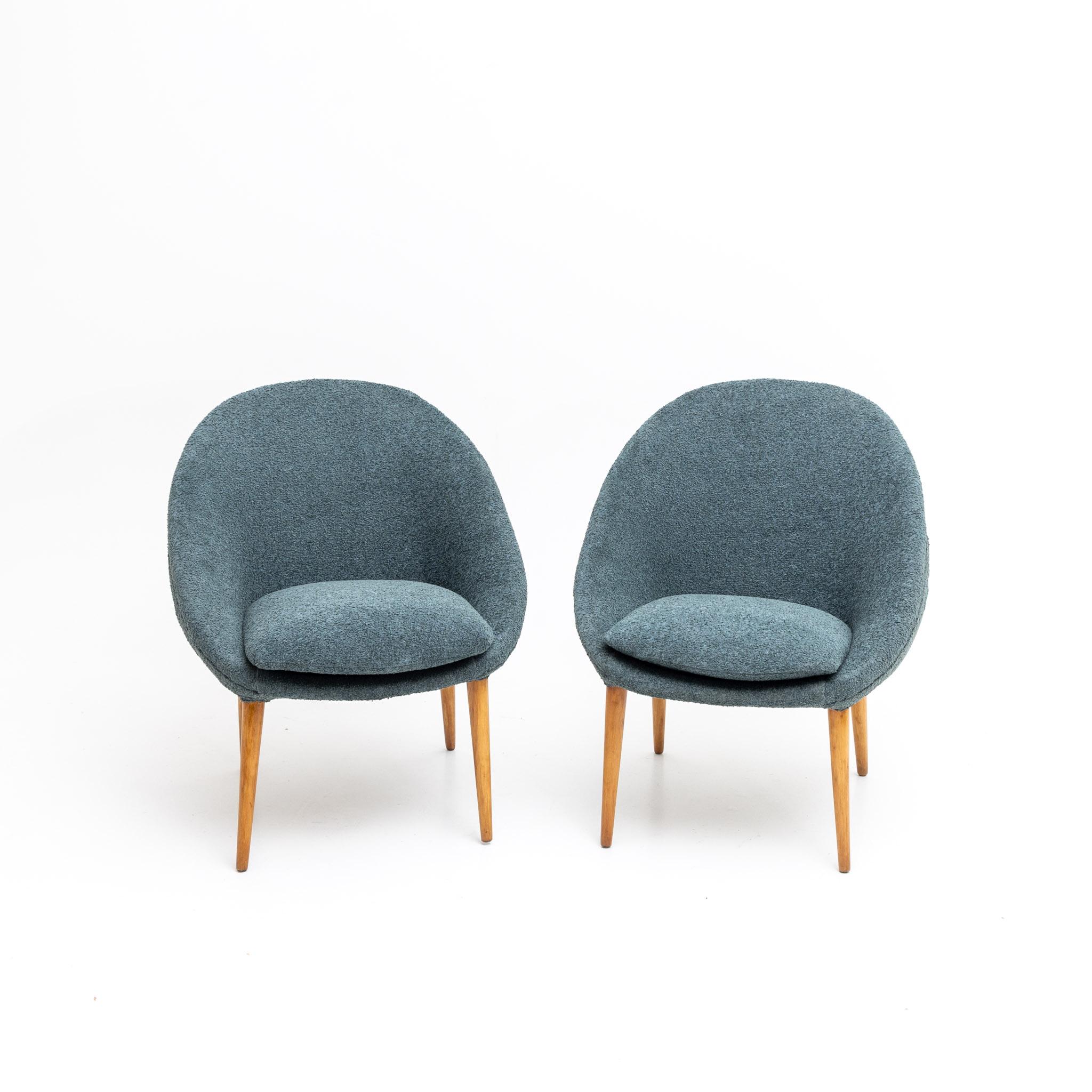 Pair of armchairs with rounded blue upholstered seat shells with cushions on conical pointed feet.