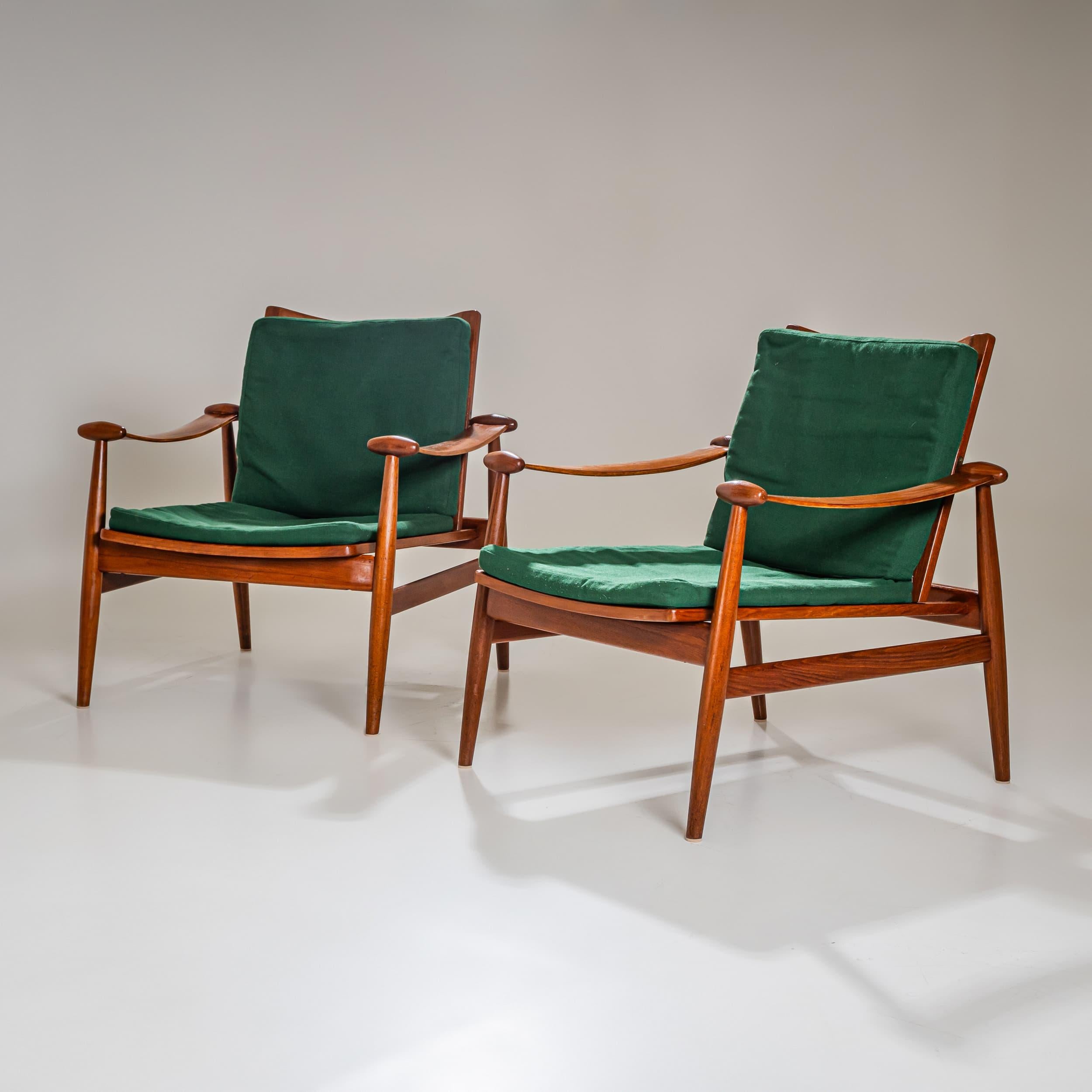 Iconic pair of armchairs by Danish designer Finn Juhl, model 133, crafted from teak wood. Distinctive features include the broad, gracefully curved armrests with prominent oval end details. The seats are strung with plastic cord and fitted with