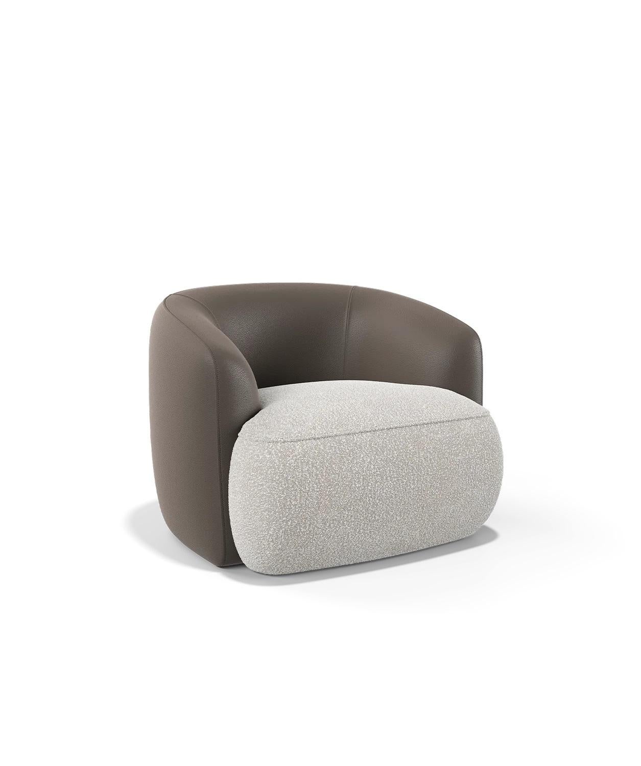 This set of two armchairs is defined by its fluid, curved silhouette, designed to offer a sense of embrace and comfort. The smooth leather envelops the back and arms, accentuating the armchair's softly contoured form, while the textured fabric seat