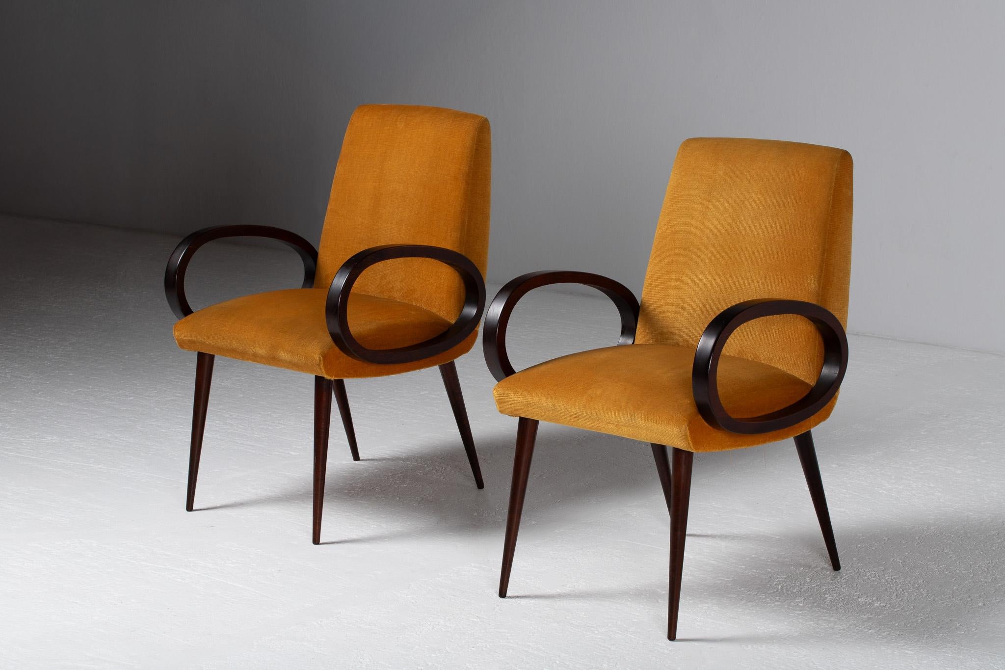 Pair of Armchairs with Loop Arms in Walnut and Ochre Velvet, Italy, 1950

Like silhouettes drawn in a single fluid gesture, this pair of Italian armchairs captures the poetics of postwar design in motion. Their elliptical arms, sculpted in dark