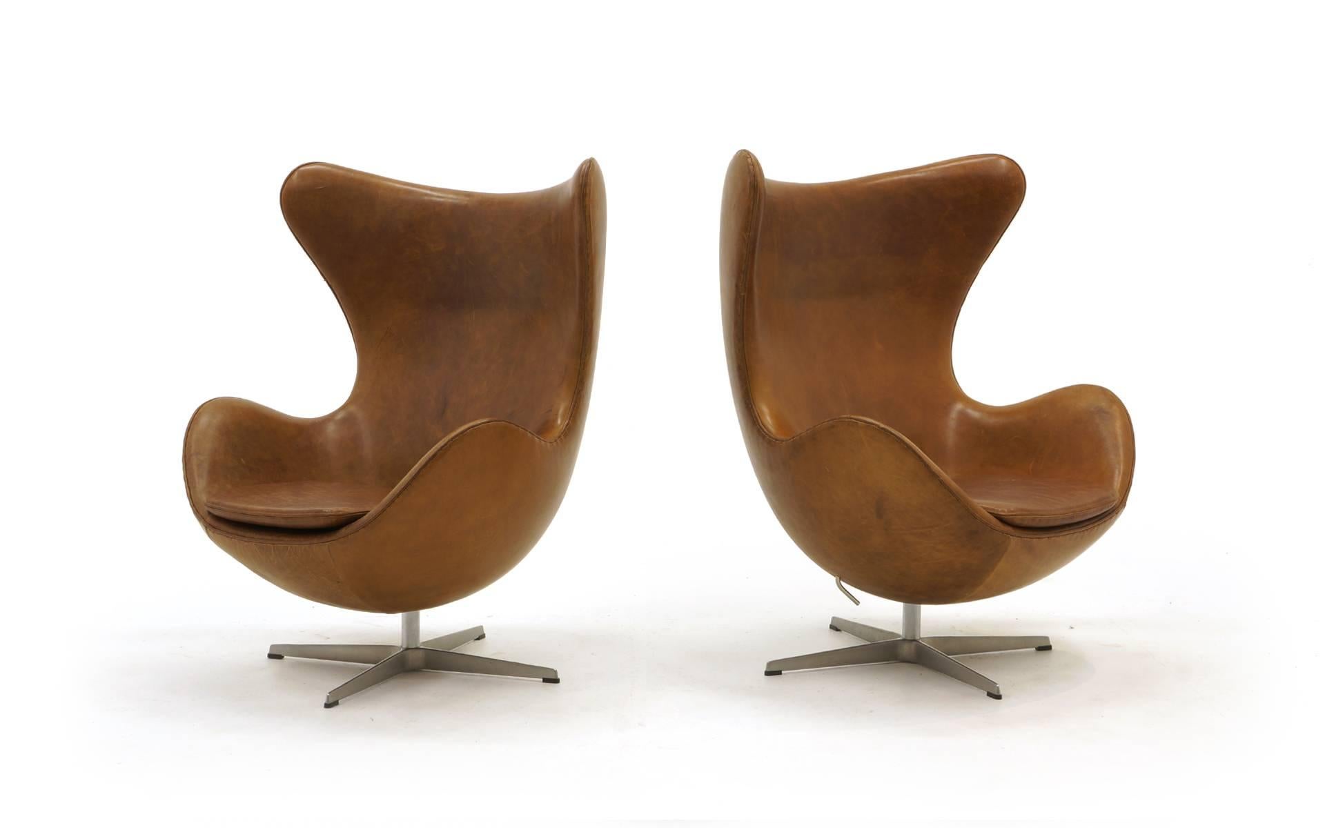 Original pair of Egg chairs designed by Arne Jacobsen. Expertly reupholstered in Moore and Giles Brentwood Cuervo leather. The inherent characteristics of this expensive leather is that it will show distress. The color fluctuations are natural to