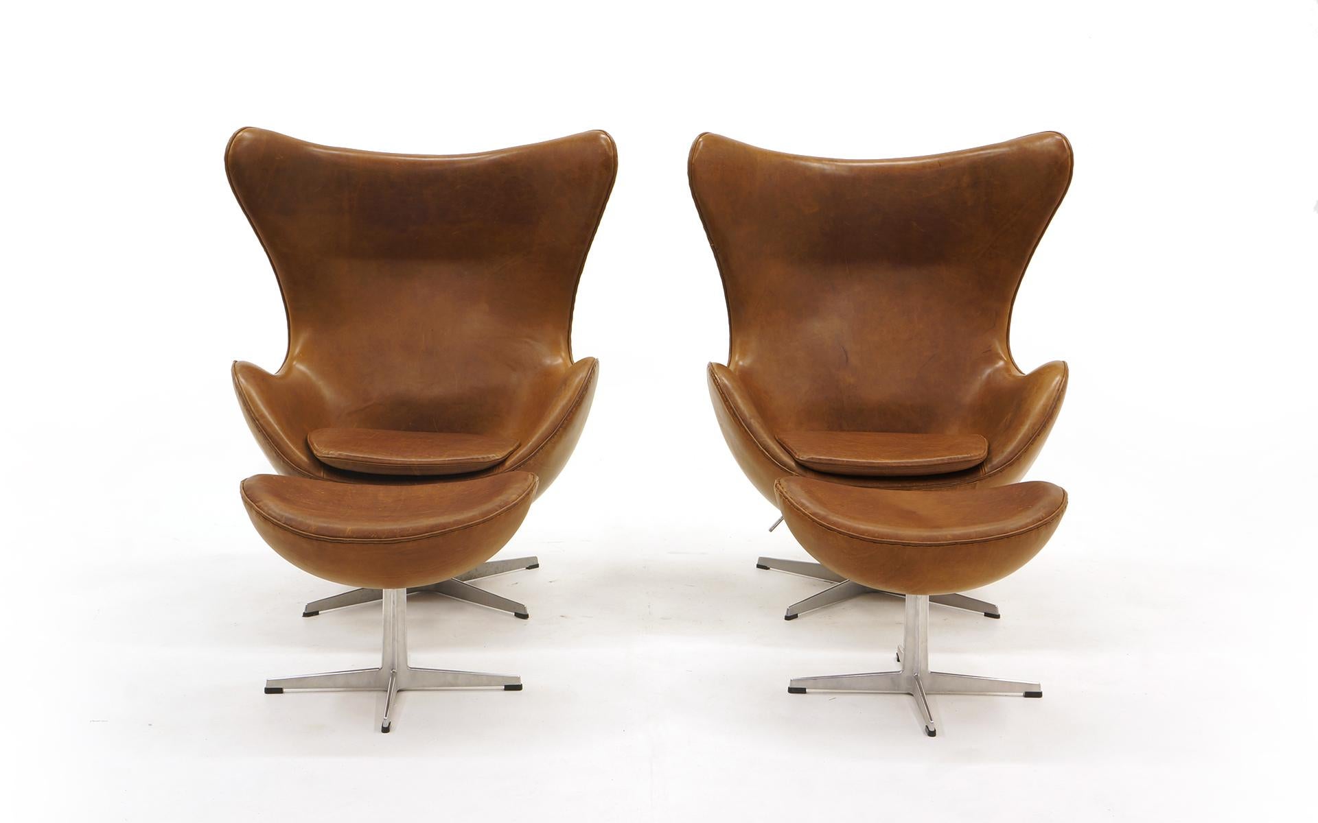 Pair of swivel tilt egg chairs and ottomans designed by Arne Jacobsen and manufactured by Fritz Hansen, Denmark. Jacobsen's modern take on the wingback lounge chair. The tilt mechanism is adjustable. The set is from the early 2000s and have been