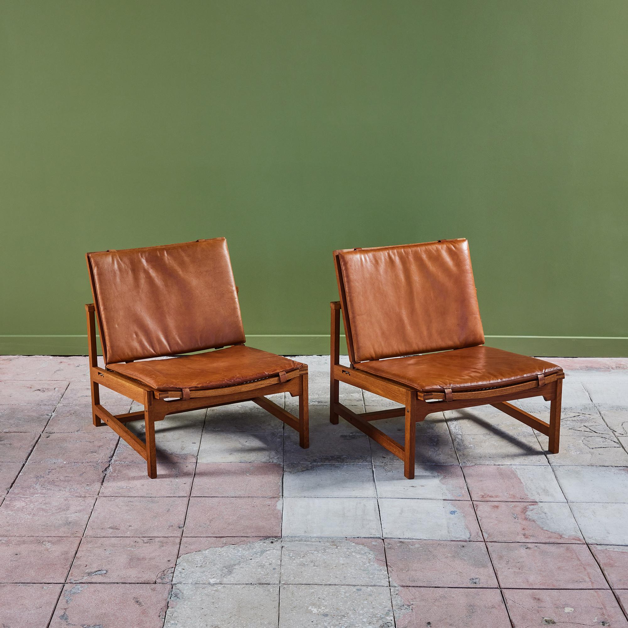 Rare pair of oak and leather lounge chairs by Arne Karlsen and Peter Hjort, for Interna, c.1960s. These chairs feature adjustable seat backs and an oak frame. The cane seat and seat backs both have the original cognac leather
