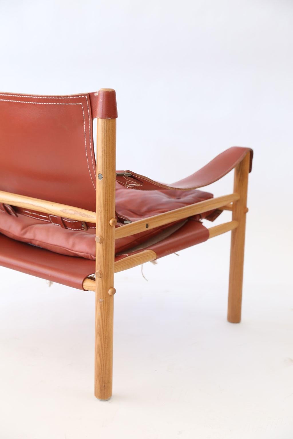 Pair of Arne Norell Sirocco chairs, collapsible safari lounge chairs fabricated by Norell Møbel AB (1964, Aneby Sweden) in light ashwood using dowel and red leather strap construction.