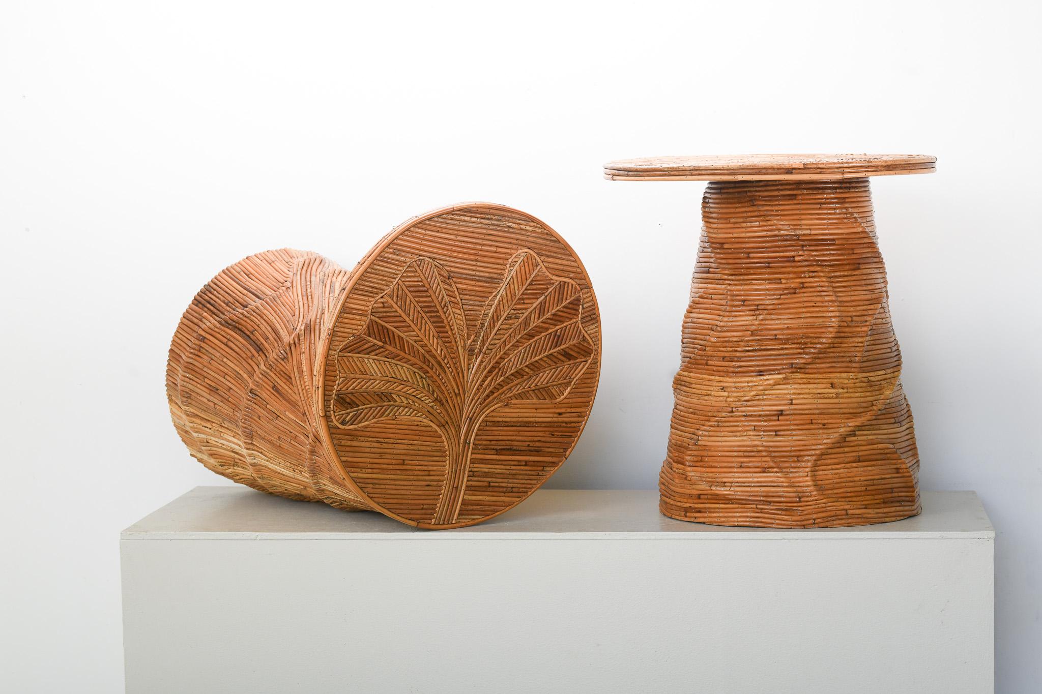 Il tavolino in rattan organico 'Arra', graziosamente bilanciato, è disponibile in coppia. Caratterizzato da una base a tamburo, con rattan intricato e motivi organici di foglie e fiori. La splendida texture naturale mette in evidenza l'arte ludica