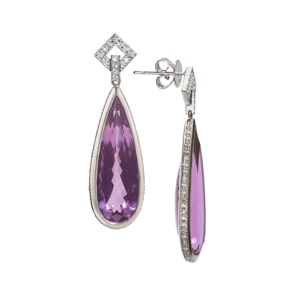 An Art Deco inspired beautiful pair of Amethyst and Diamonds Drop Earrings.
The pair of faceted elongated fine purple amethysts in white gold bezel unusually set with round diamonds seen from the side of the earring. The drops are suspended from