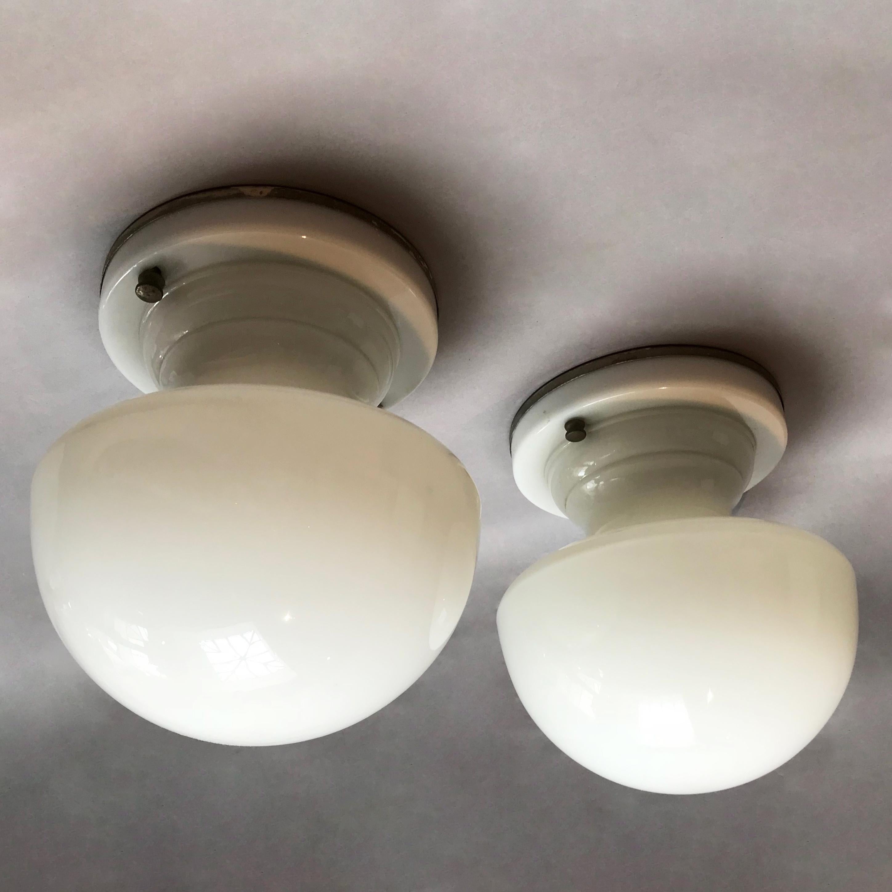 Pair of rare, Art Deco, flush-mounted, ceiling lights are one piece, seamless, molded milk glass forms with metal back plates that are wired to accept up to 150 watt bulbs each. The lights can be used as wall sconces. Listed price is for the pair.