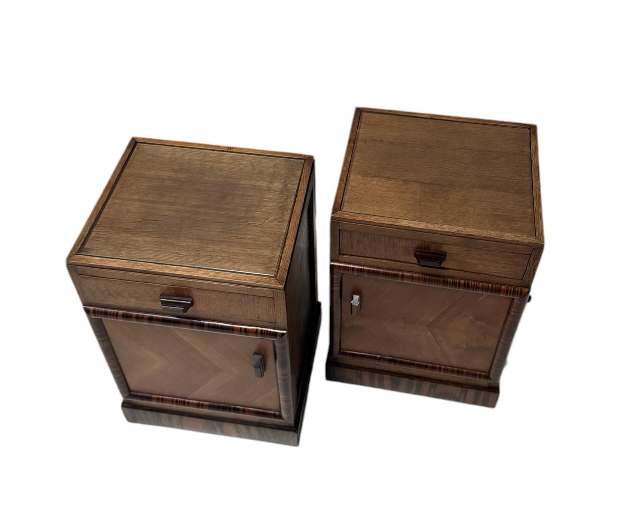 Stunning  and elegant pair of Art Deco Amsterdamse School nightstands or bedside tables.
Striking Dutch design from the 1920s.
Solid oak base with original walnut veneered doors.
Original macassar ebony veneer lining and glass tops.
This wonderful