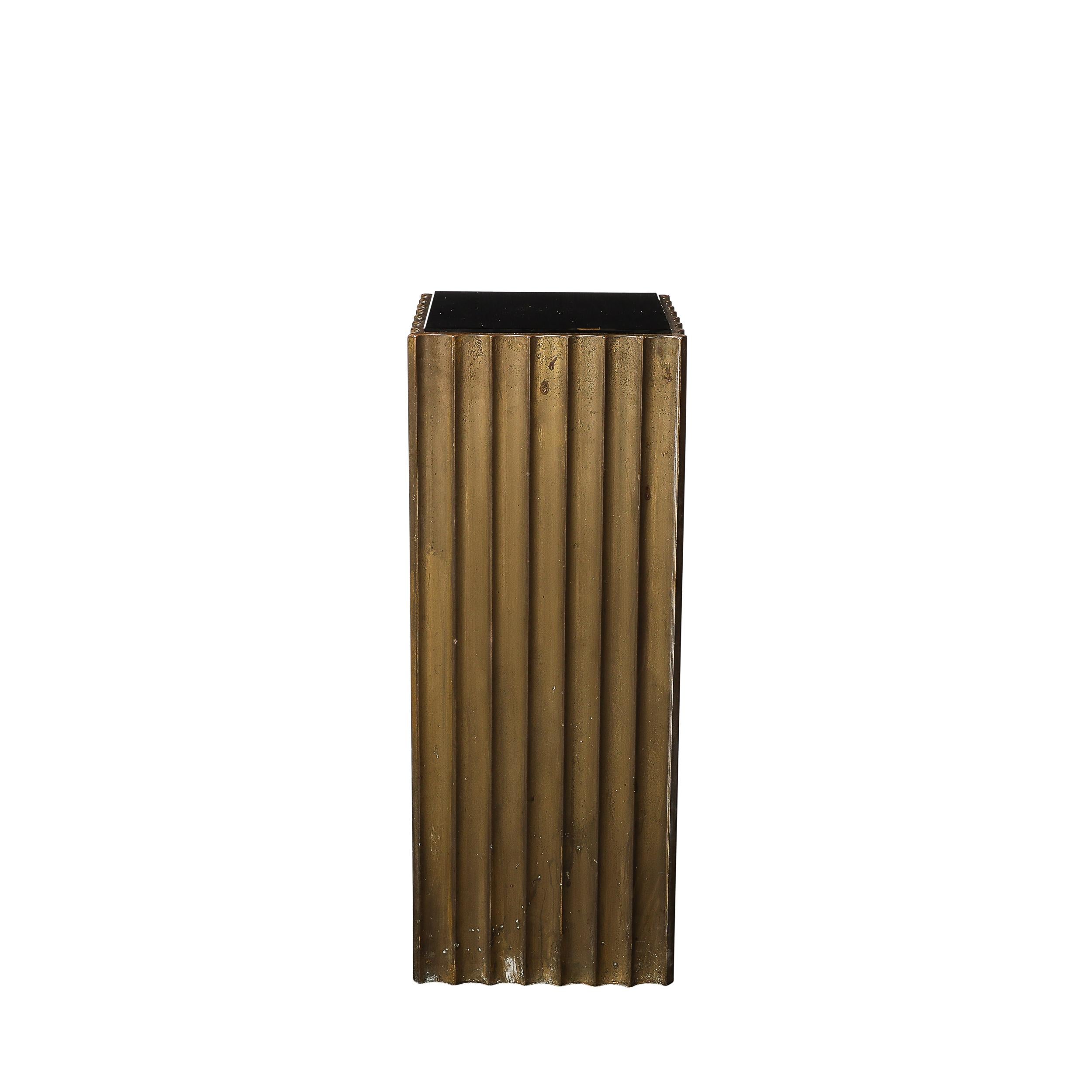 This boldly scaled pair of Art Deco Antiqued Bronze Fluted Pedestals w/ Vitrolite Tops originate from the United States, Circa 1930. They feature a substantial presence with beautiful scalloped edges achieved by vertical fluted detailing on all four