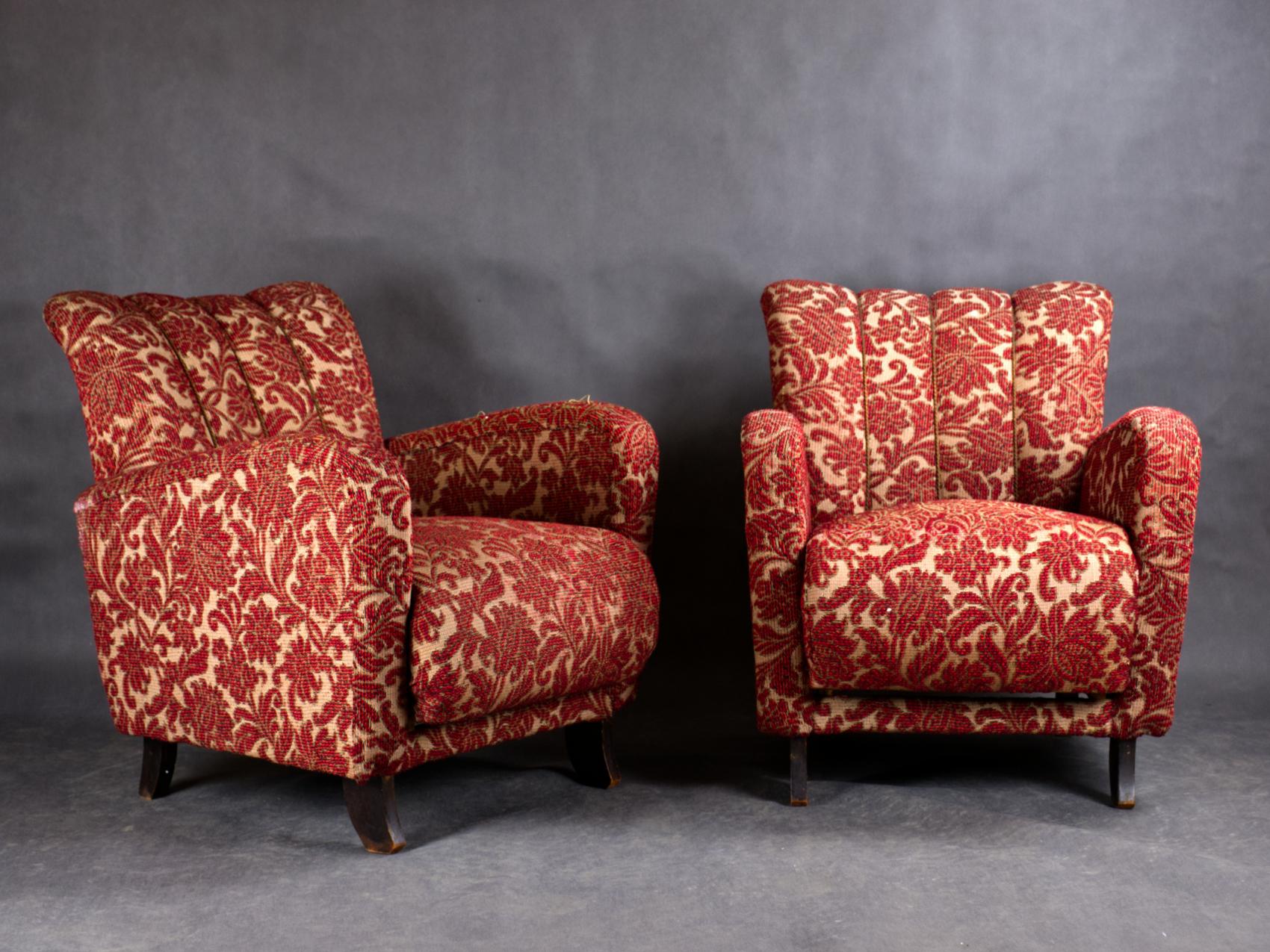These art deco chairs attributed to J. Halabala have red and gold upholstery with a floral and leaf pattern. The chairs have a classic art deco shape with rounded, comfortable backrests and curved armrests. The legs of the chairs are made of wood