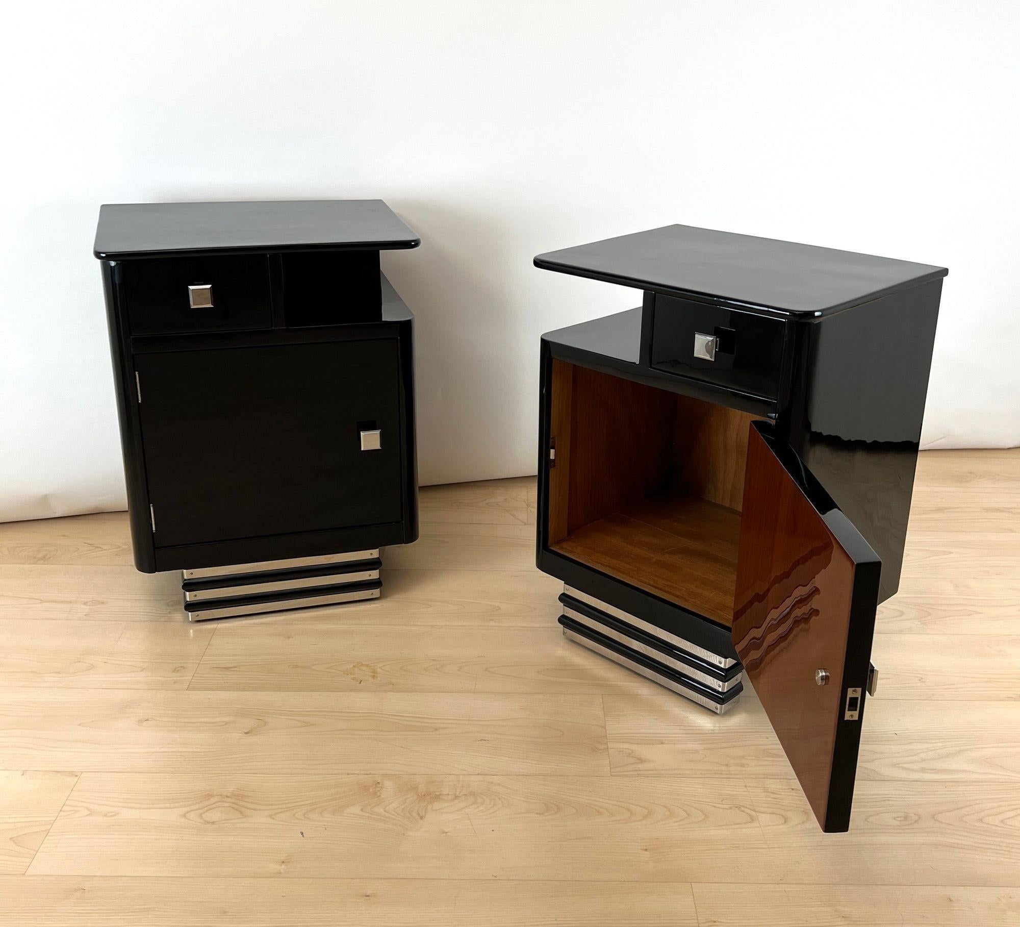 Coppia di comodini originali Art Déco completamente restaurati, provenienti dalla Francia intorno al 1930.

Noce, rivestito con lacca nera per pianoforte e lucidato a specchio. Tre strisce decorative in acciaio inox lucido sulla base.
Un cassetto