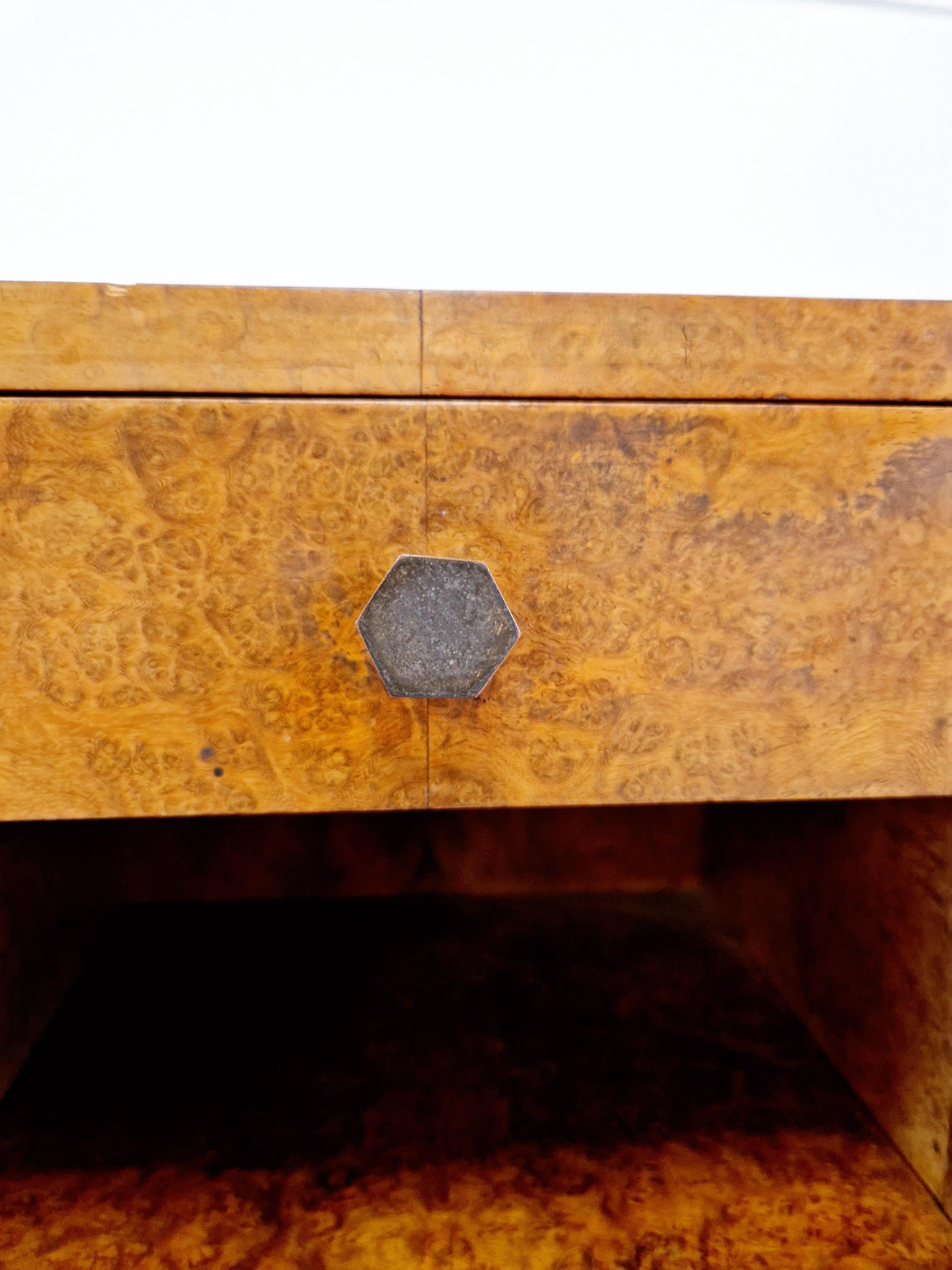 This pair of Art Deco walnut burr bedside cabinets from the 1930s exudes a sense of elegance and sophistication. Made from solid wood with a fabulous walnut burr veneer and a matte handle finish, these nightstands feature two drawers and an embossed