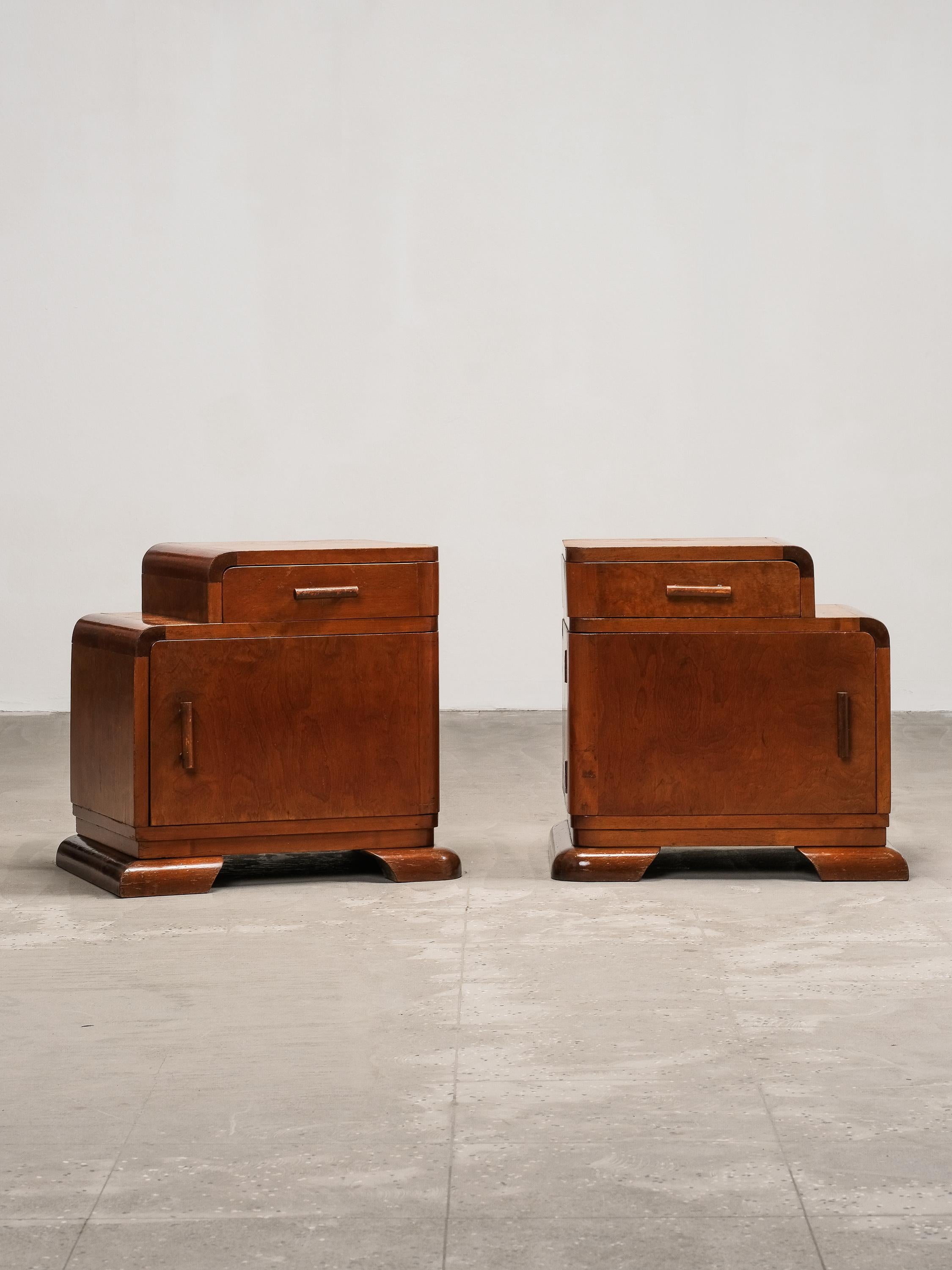 A beautifully preserved pair of Art Deco bedside tables, most likely crafted in France during the 1930s. These pieces reflect the era’s bold yet refined design ethos, combining functionality with sculptural form.

Each table features a stepped top