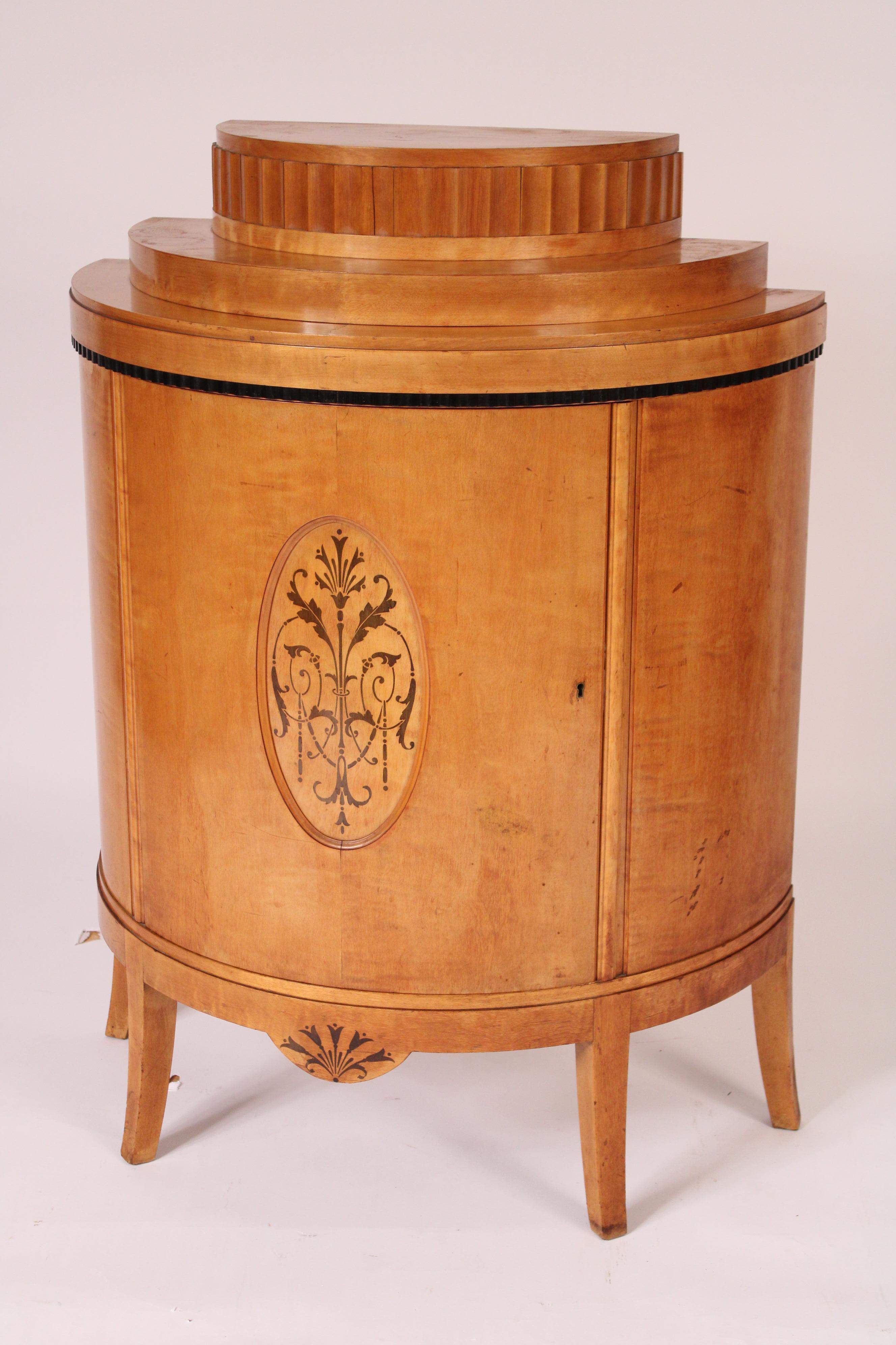 Coppia di armadietti demi lune in betulla art déco, anni '30 circa.  Con un piano in demi lune graduato a tre gradini, un'anta sagomata in demi lune intarsiata, un grembiule con intarsio centrale a campanula, gambe quadrate affusolate e leggermente