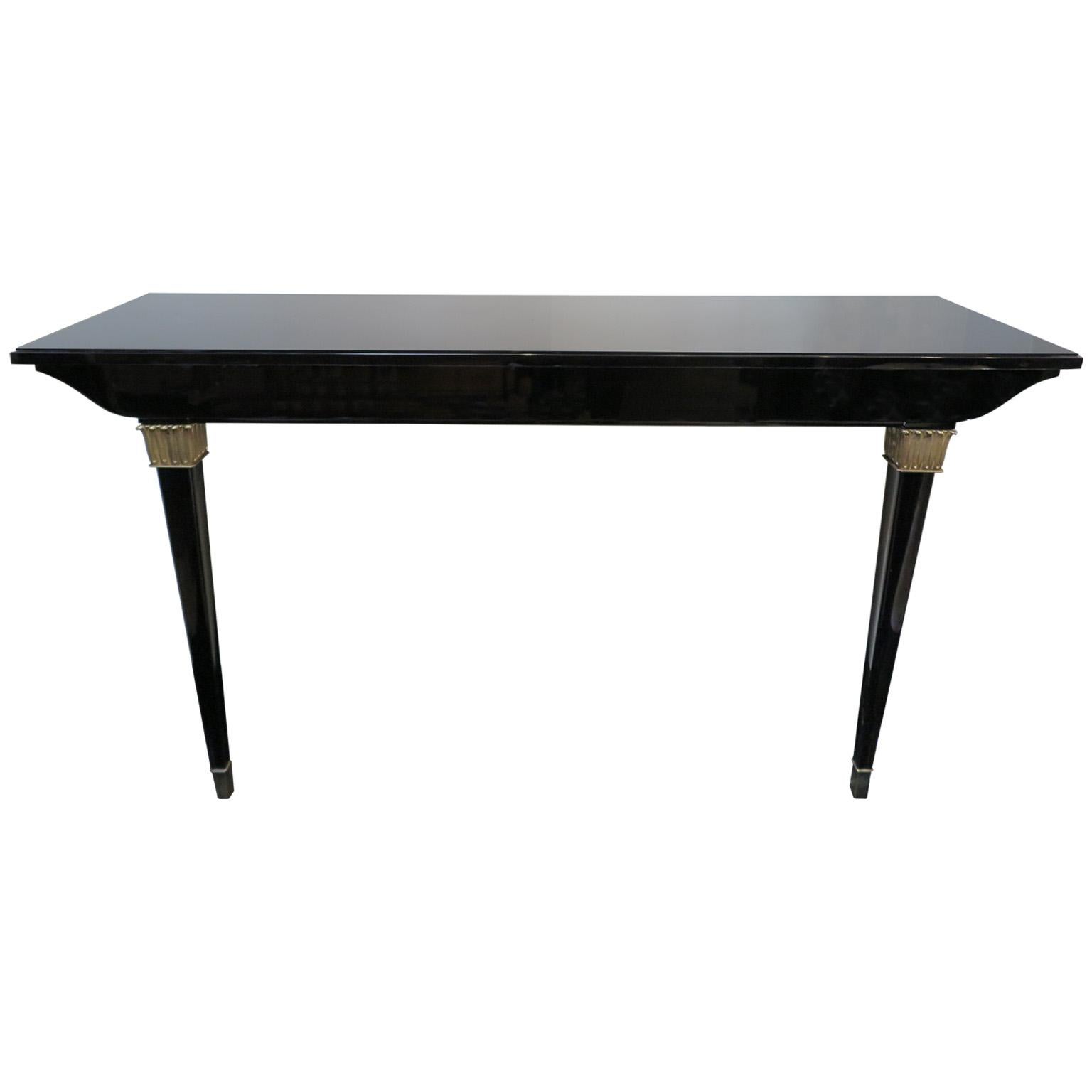 Pair of French Art Deco wall mounted consoles with black lacquer frame in a gloss finish. The two front legs feature two square brass relief accents with stylized leaves. The thick apron top showcases curved sides. A black glass sits onto of the